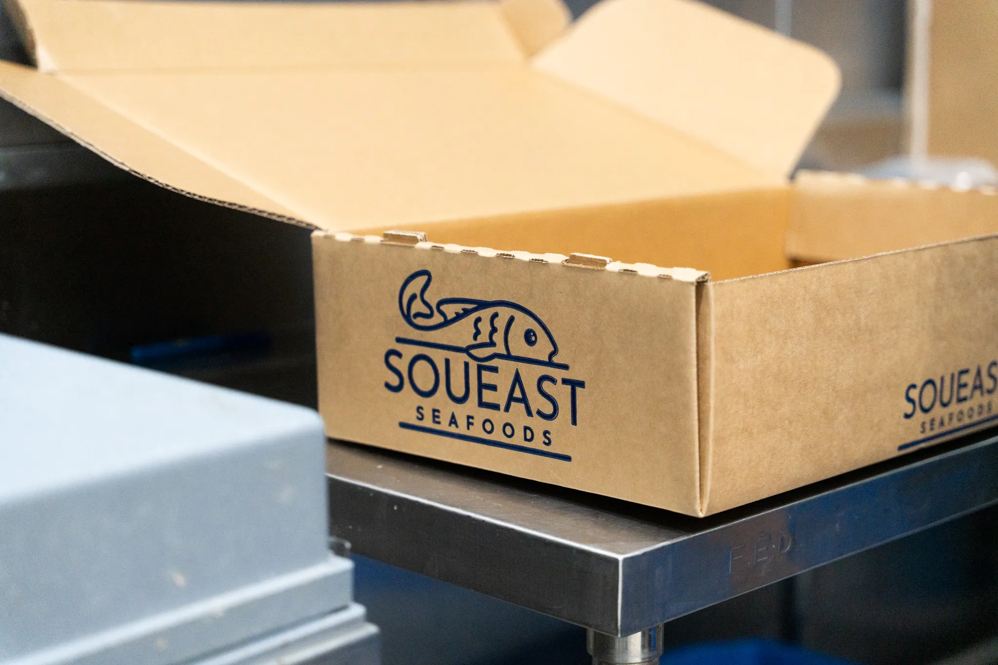 Open cardboard box with Squeast Seafoods logo and fish illustration on a metal table.