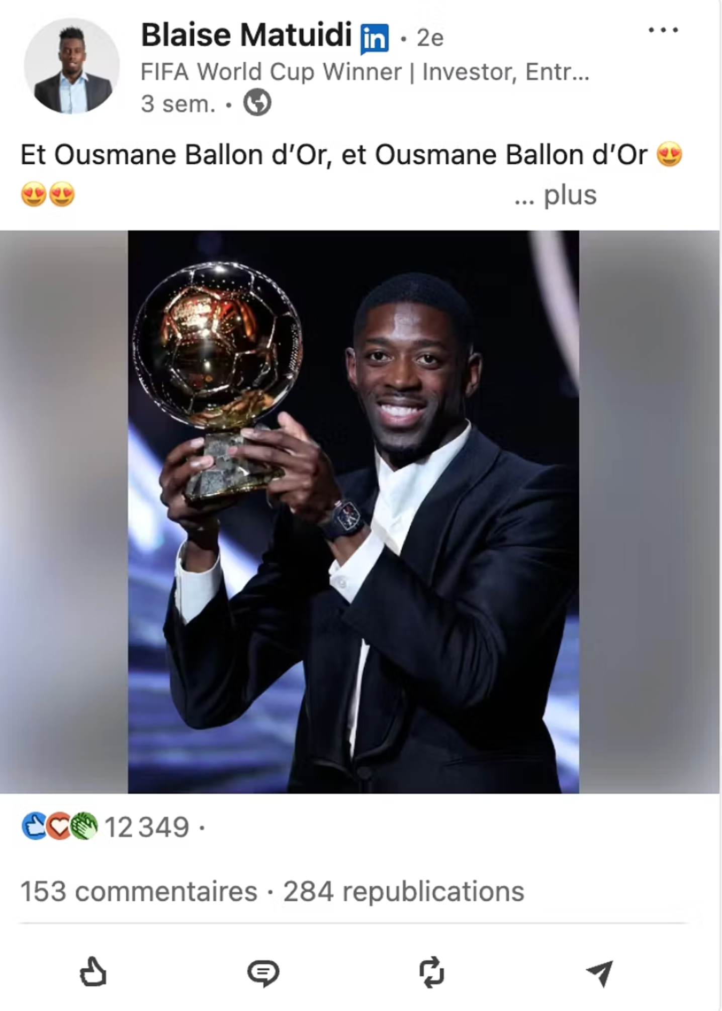 Ousmane Dembélé smiling and holding the Ballon d'Or trophy dressed in a black suit and white shirt.