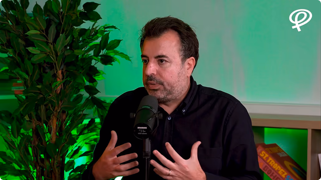 Homme parlant devant un microphone avec des plantes et des livres en arrière-plan vert.