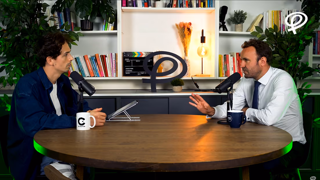 Deux hommes discutent avec microphones devant une bibliothèque dans un studio d'enregistrement.