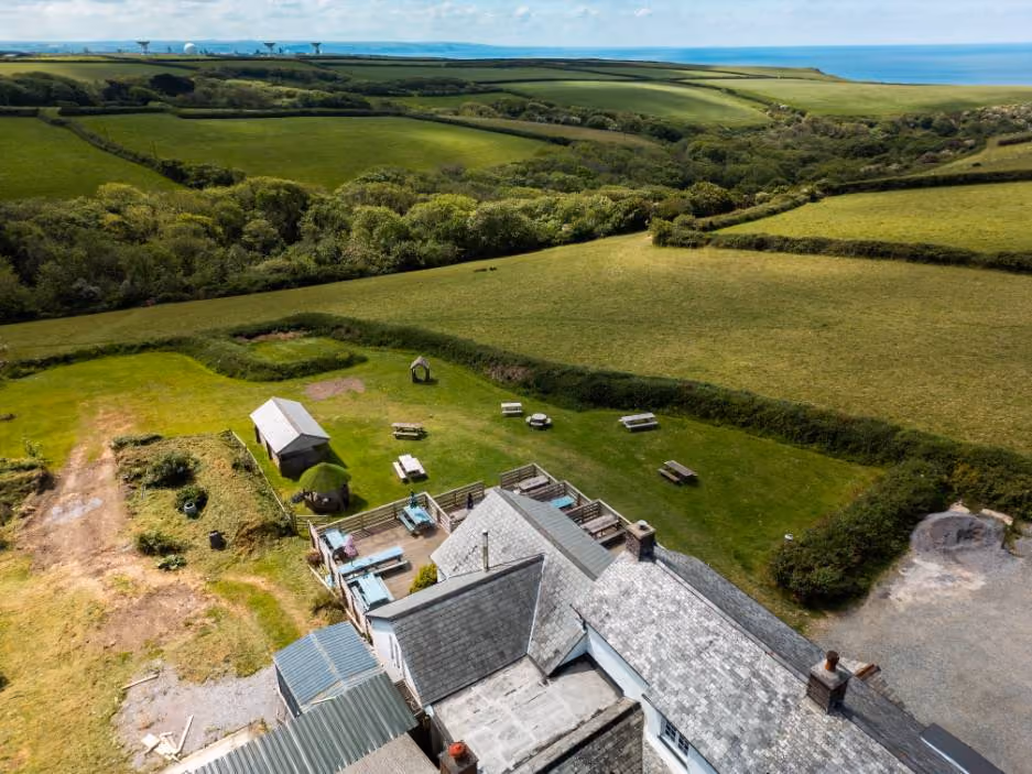 Aerial view of countryside landscape with green fields, picnic tables, and a building with a gray roof.