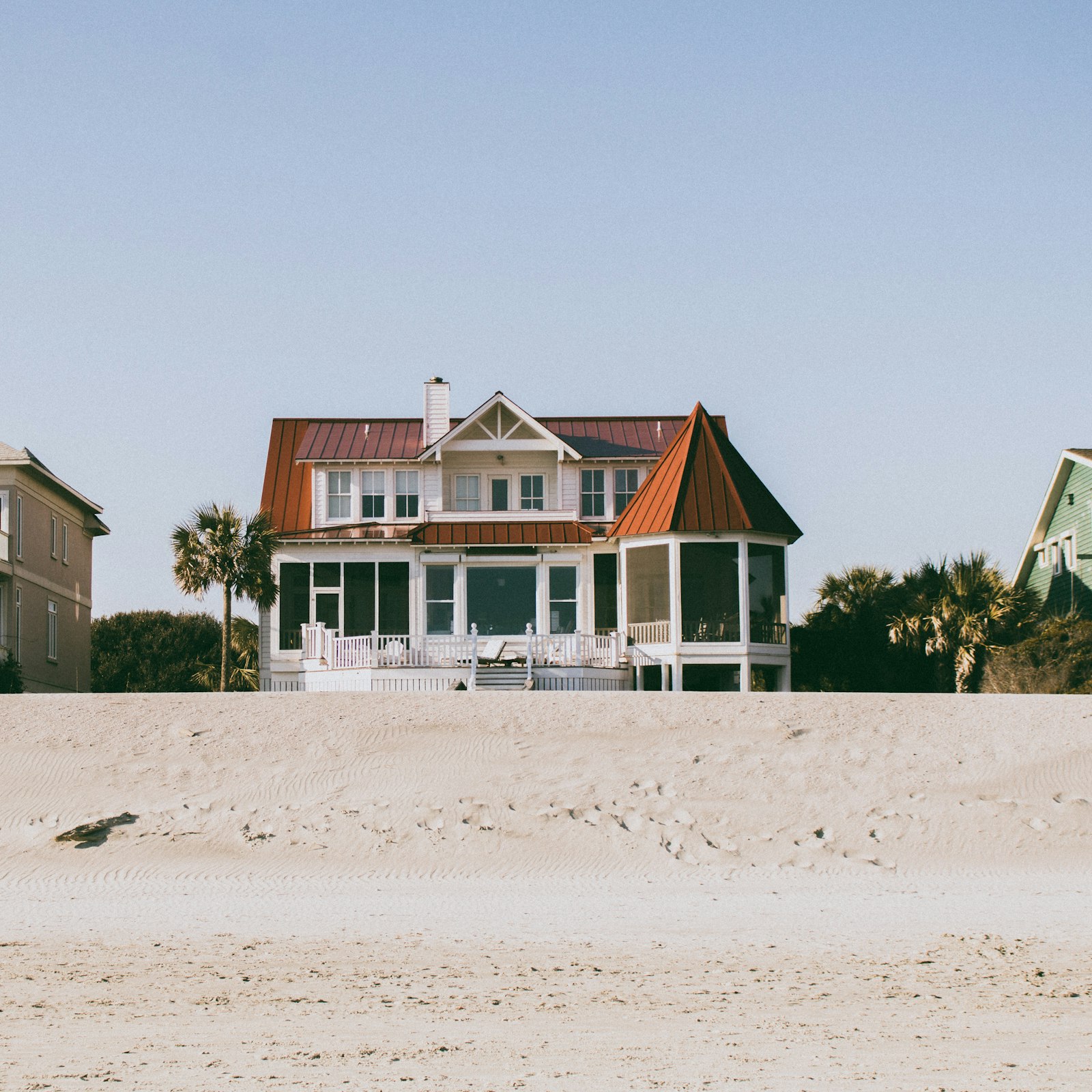 White and brown two-story wooden beach house with palm trees