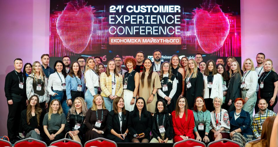 Групове фото спікерів та учасників 21-ї Customer Experience Conference на сцені перед екраном конференції.