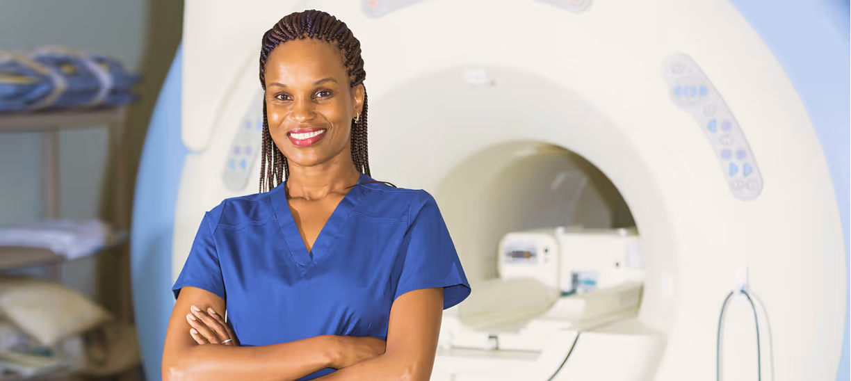MRI radiographer / technologist standing confidently in front of an MRI scanner 