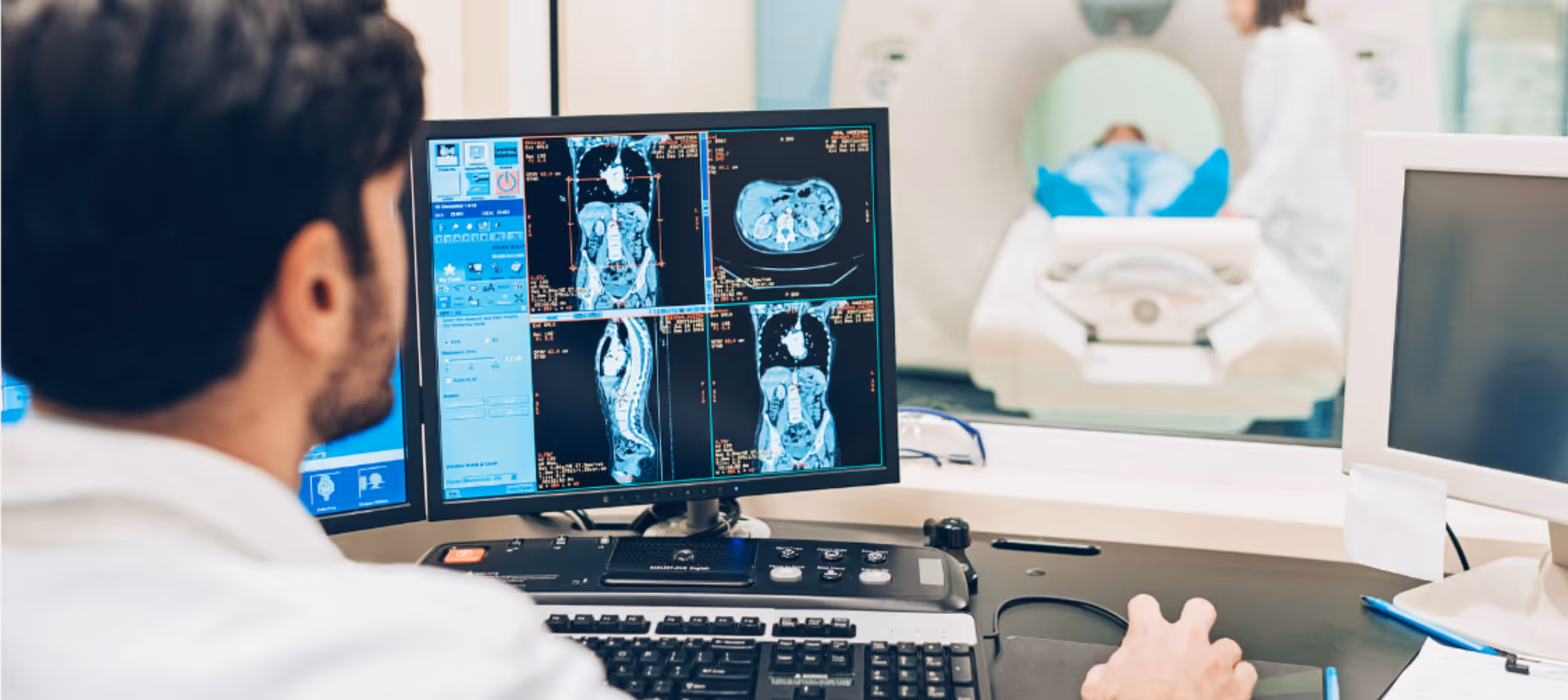 An MRI radiographer / technologist planning an MRI protocol on his scanner console, while a radiology technical aide is helping position the patient in the MRI scanner
