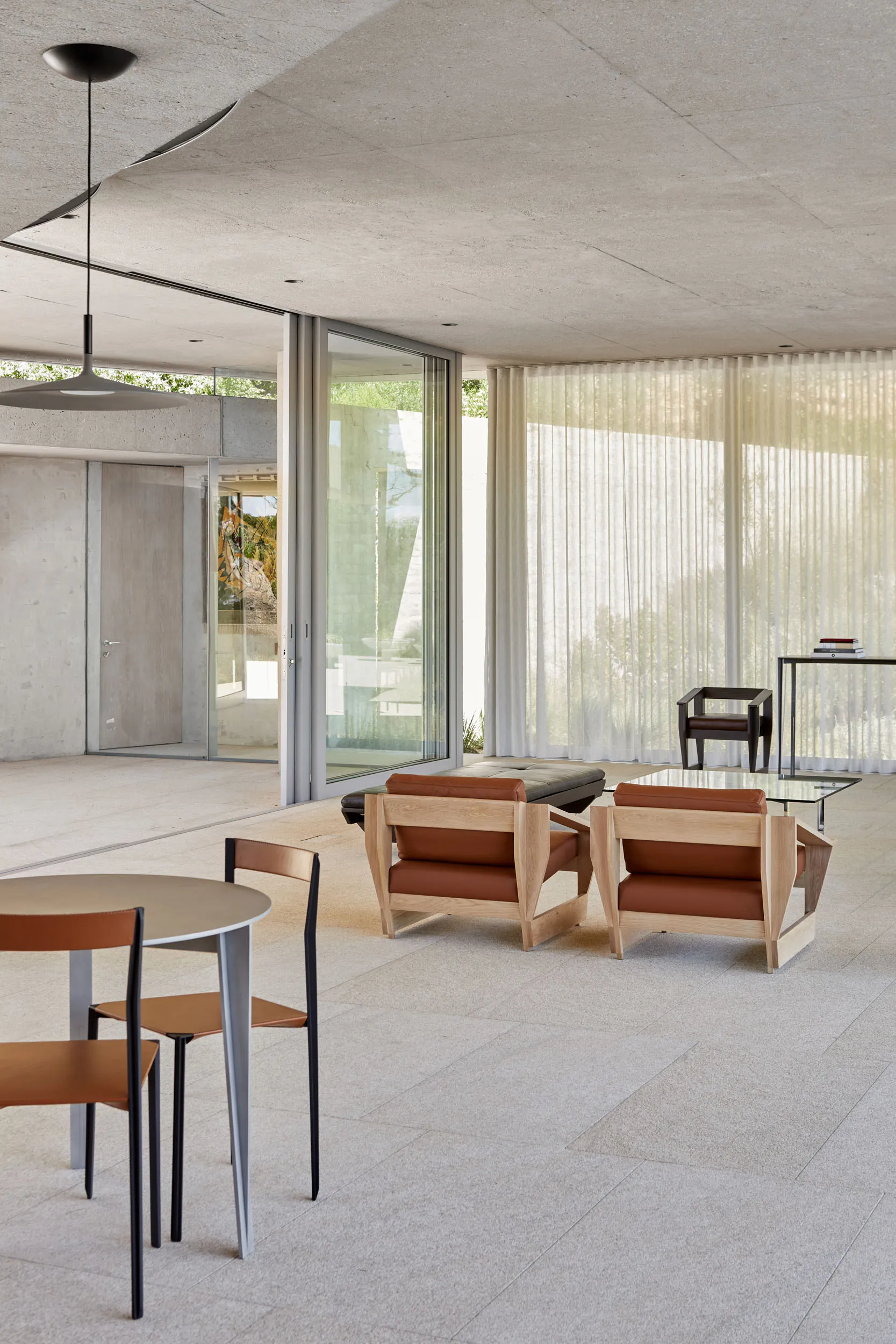 Minimalist indoor seating area with two leather chairs, a table with chairs, and large glass doors.