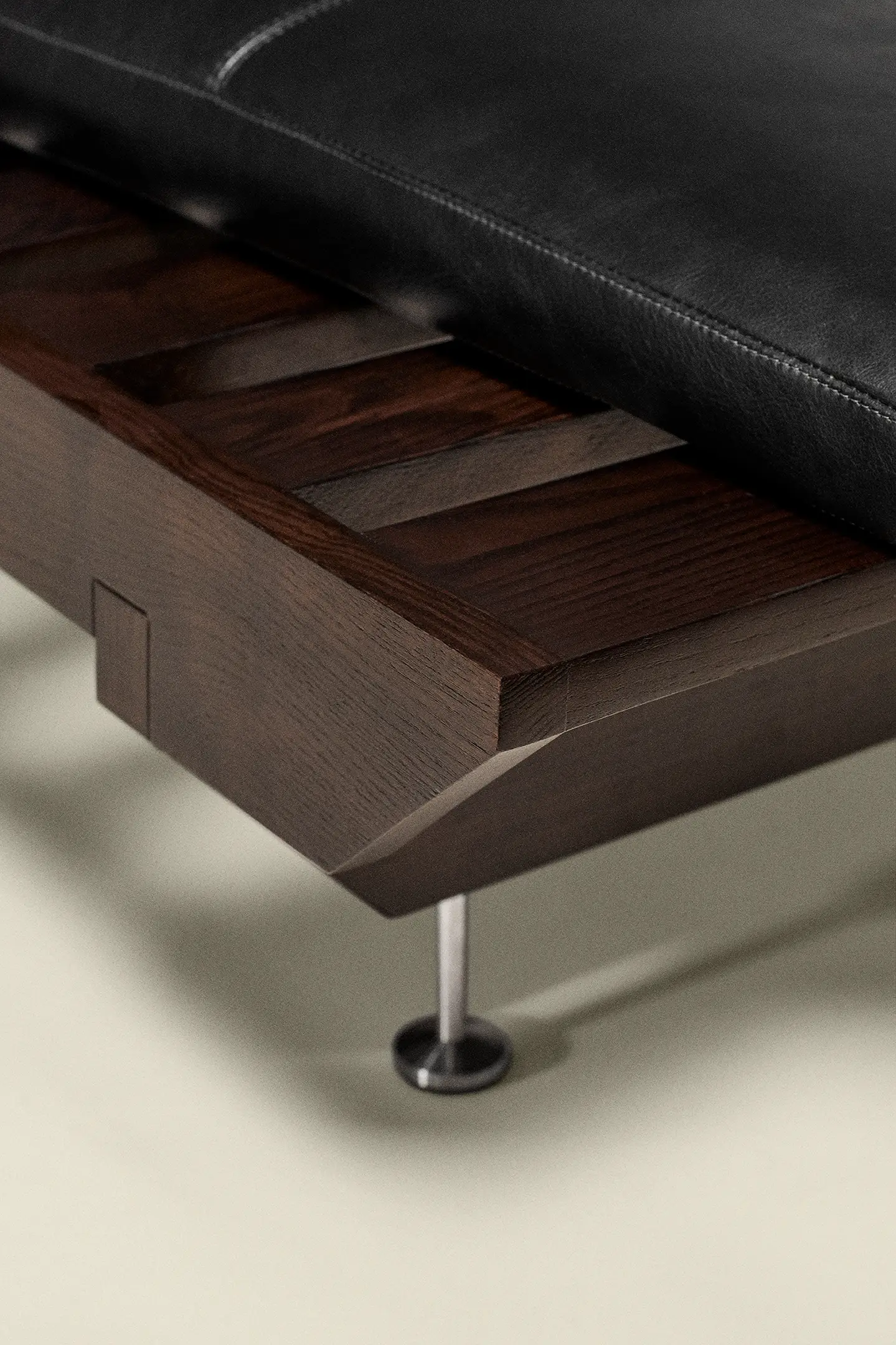Close-up of a dark wood frame daybed with a black leather cushion and metal leg on cream floor.