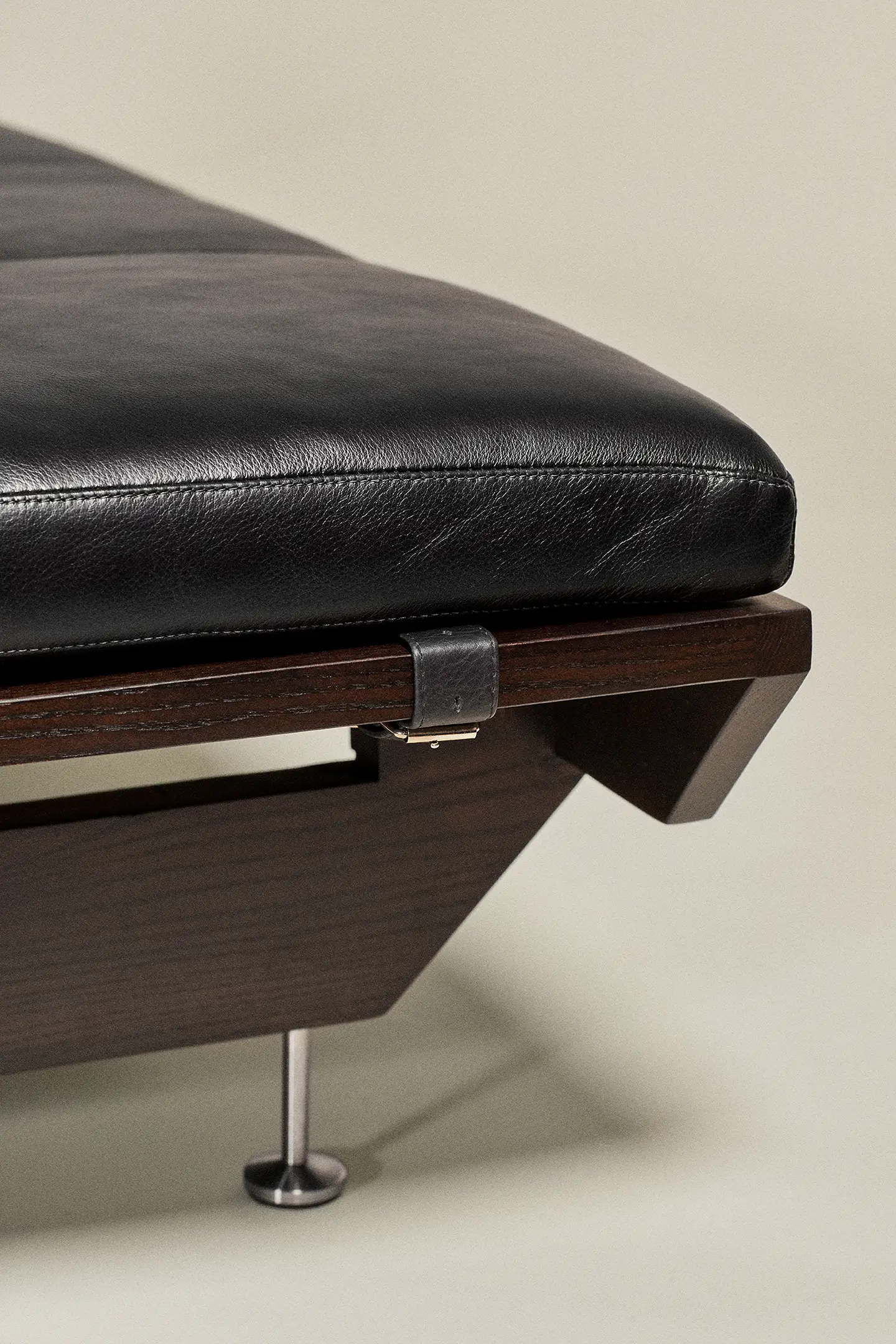 Close-up of a black leather cushion on a dark wooden chair frame with metal support leg.