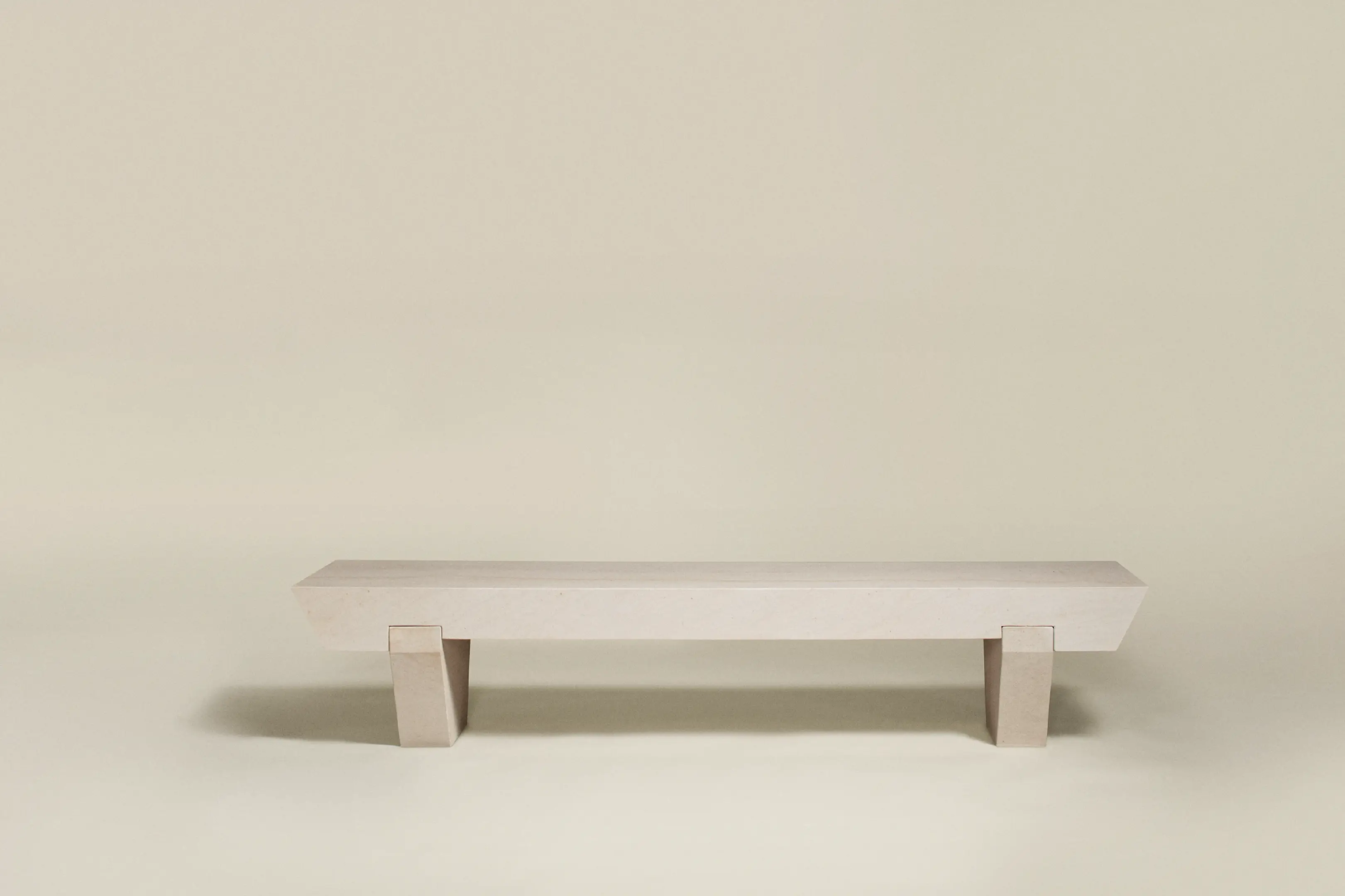 Minimalist beige stone bench with two rectangular legs on plain background.