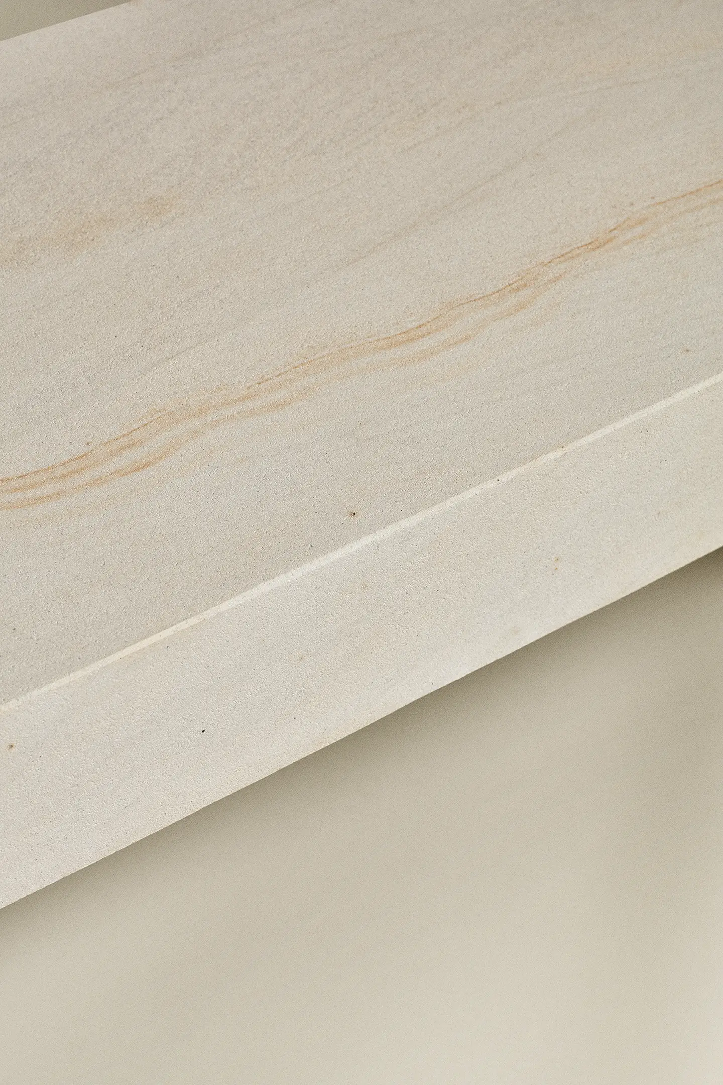 Close-up of beige stone surface with natural light brown veining and texture details.