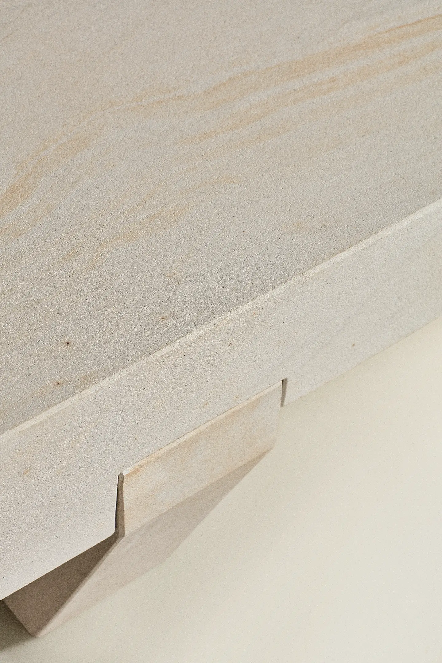Close-up of a beige stone bench edge and leg with natural texture and grain patterns.