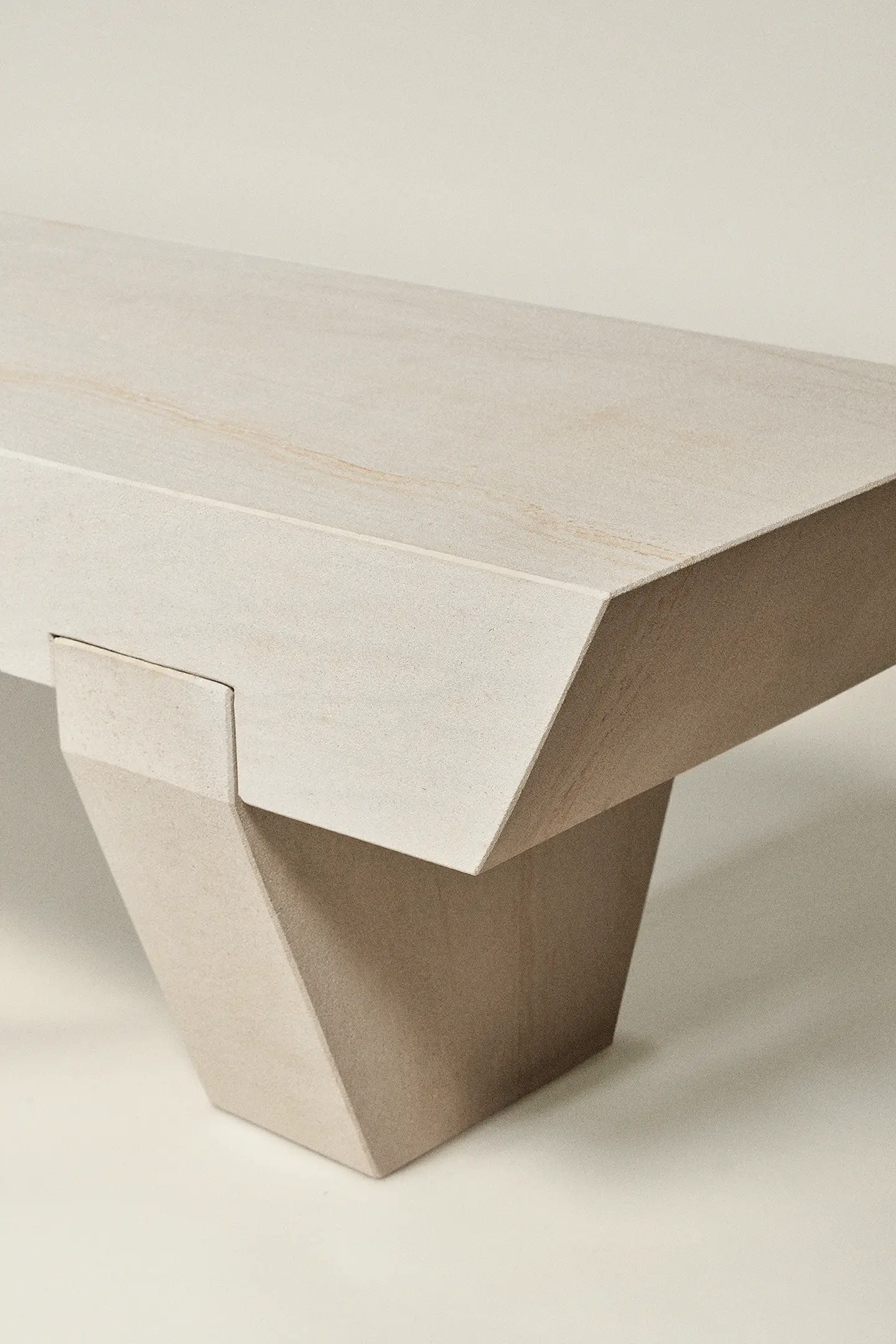 Close-up of a beige stone bench with a geometric, angled leg design.