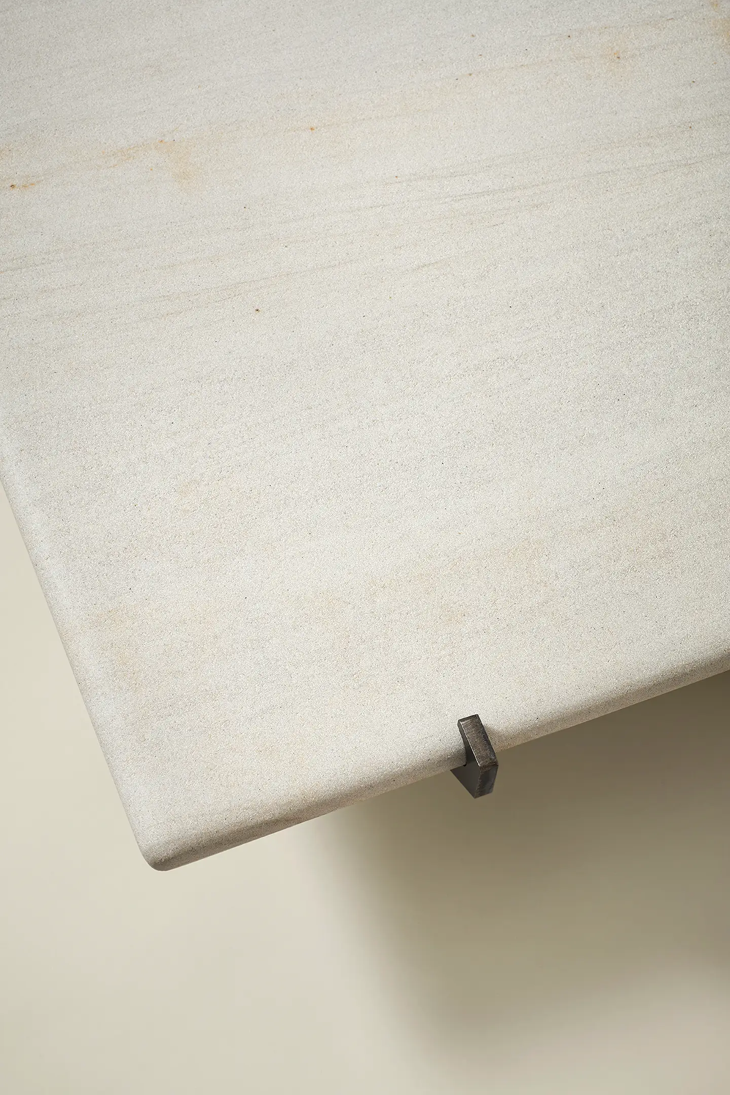 Close-up of a rectangular light beige stone coffee table corner with a small metal detail underneath.