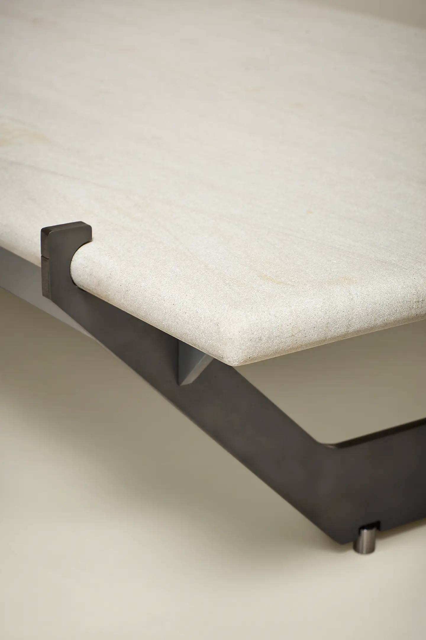 Close-up of a beige stone tabletop with a rounded edge supported by a black metal frame.