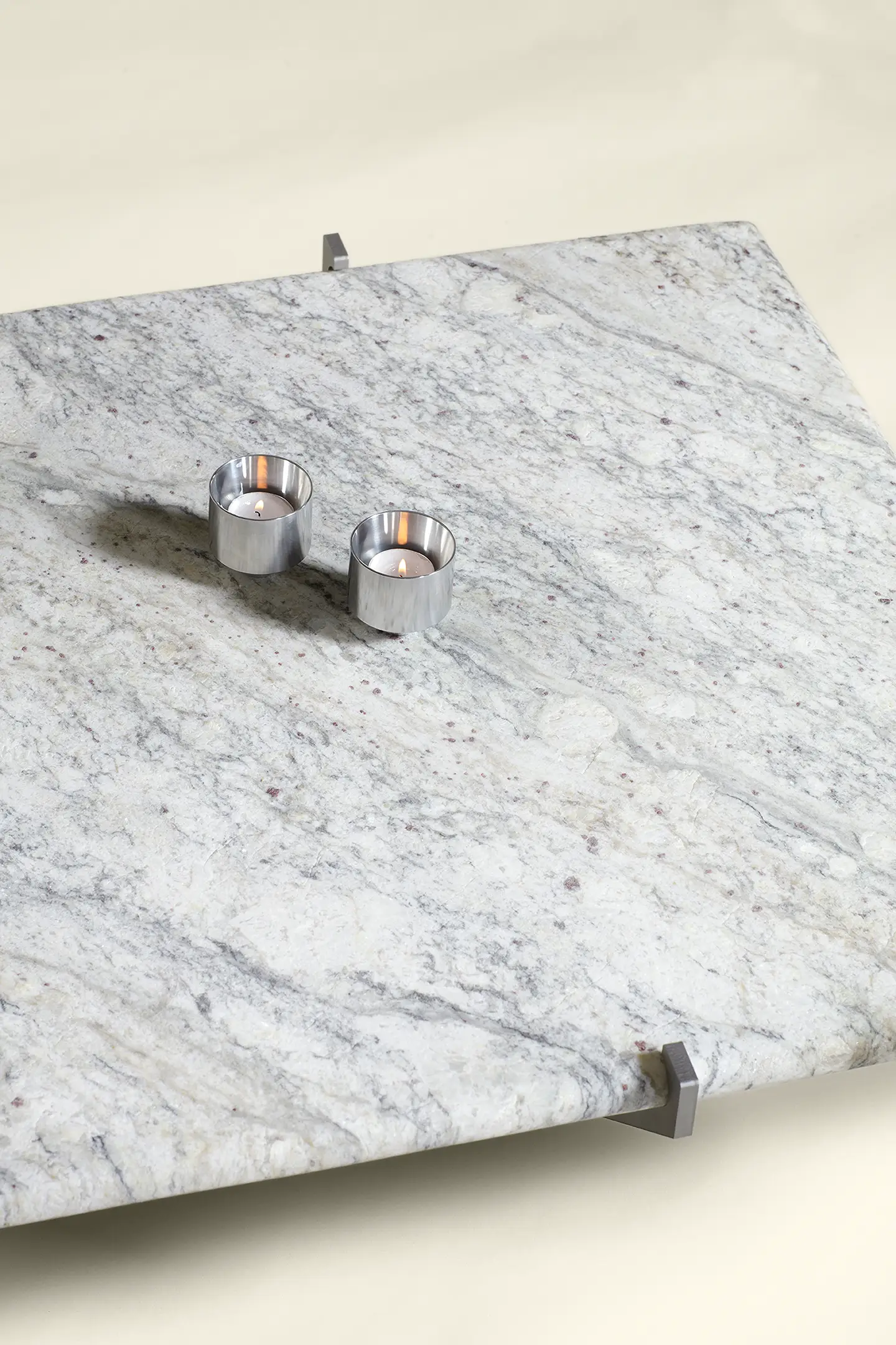 Modern square marble coffee table with two lit silver tea light candle holders on a cream background.