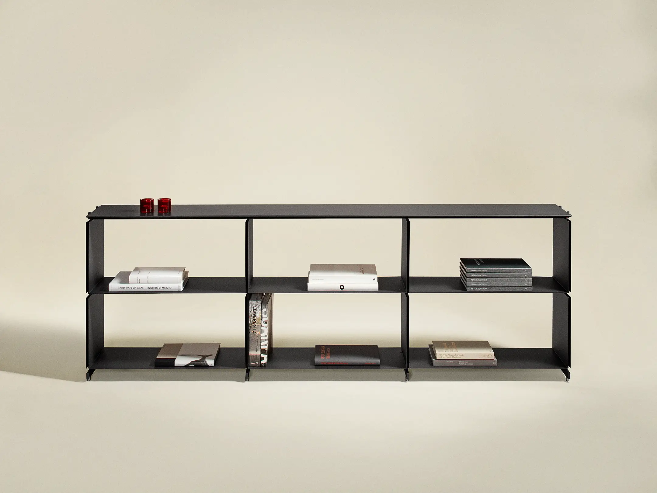 Black modern open shelving unit with books and two red tealight holders on the top shelf.