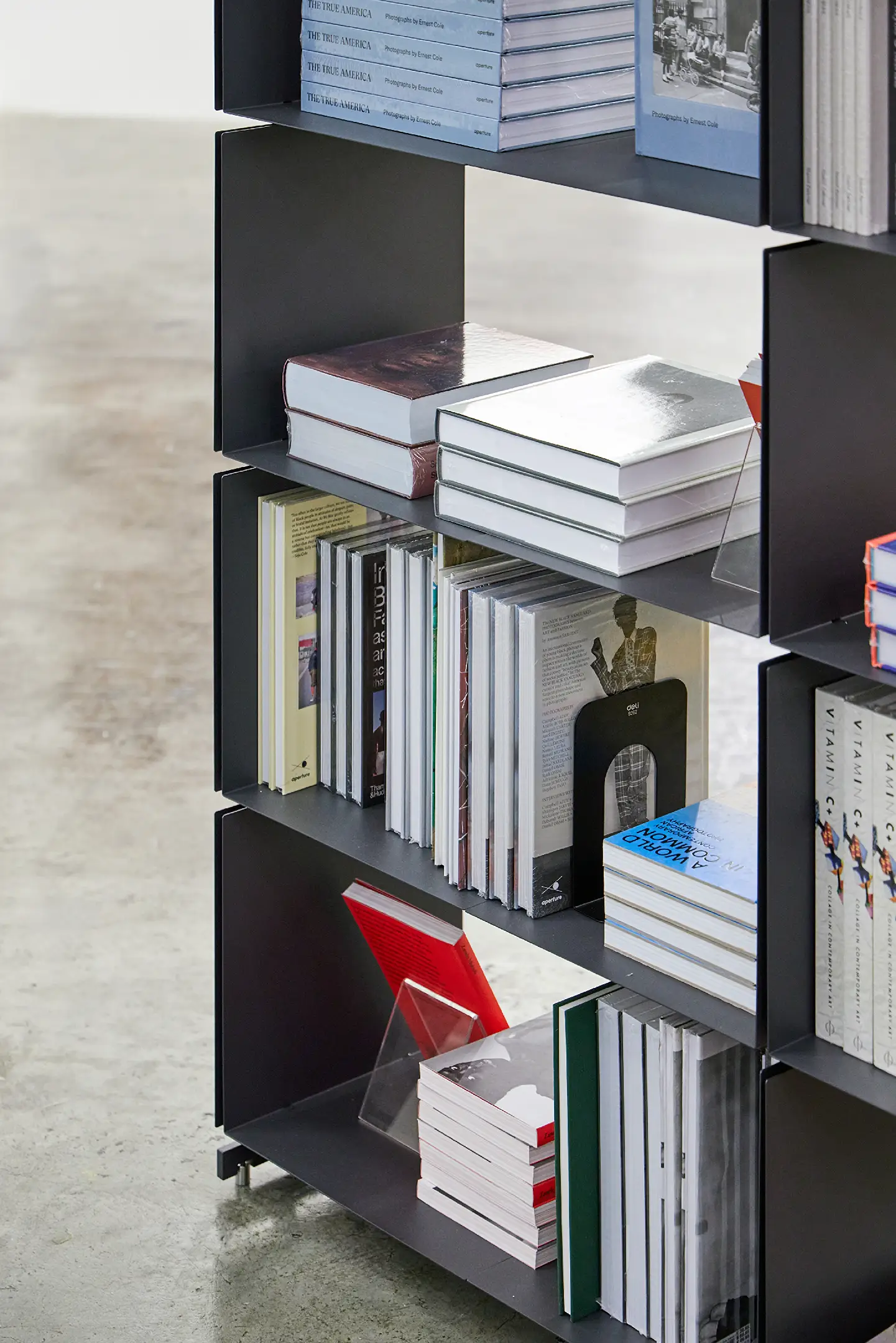 Black metal bookshelf with stacks and rows of art and photography books on concrete floor.