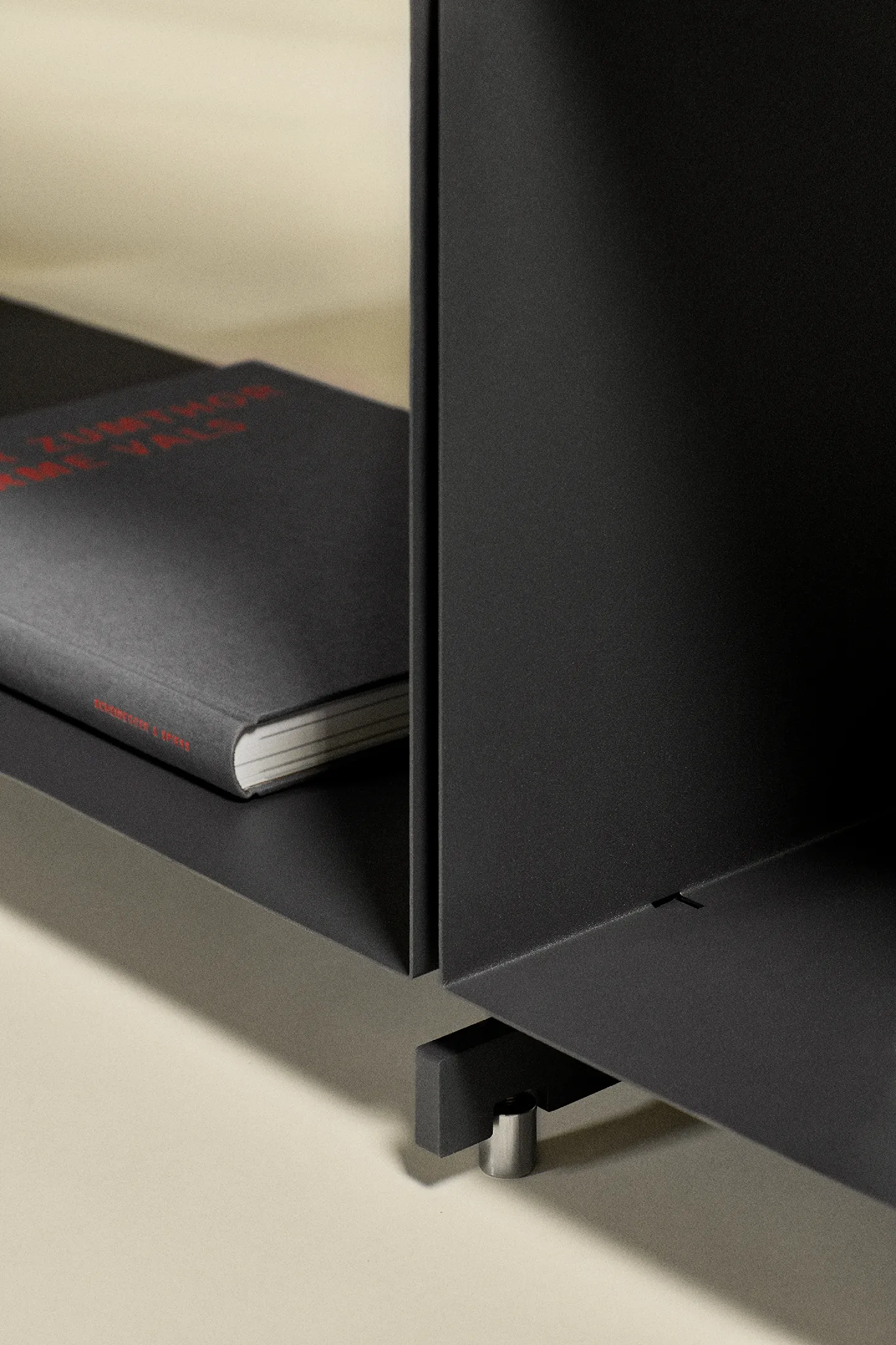 Close-up of a black metal shelf corner with a black book lying on the shelf.
