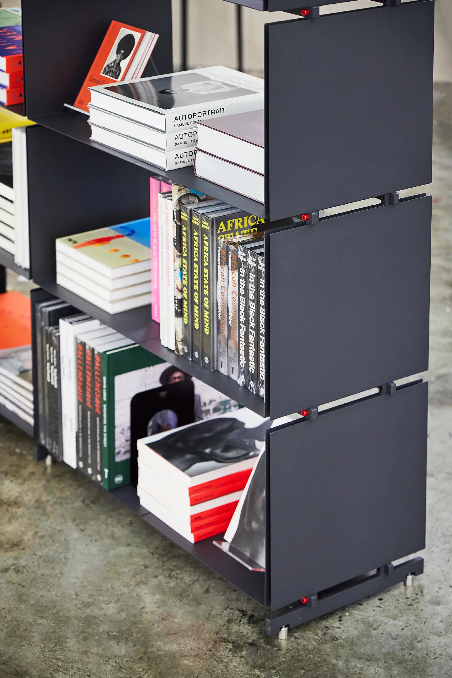 Black modular shelving unit with stacks of art and photography books on a concrete floor.