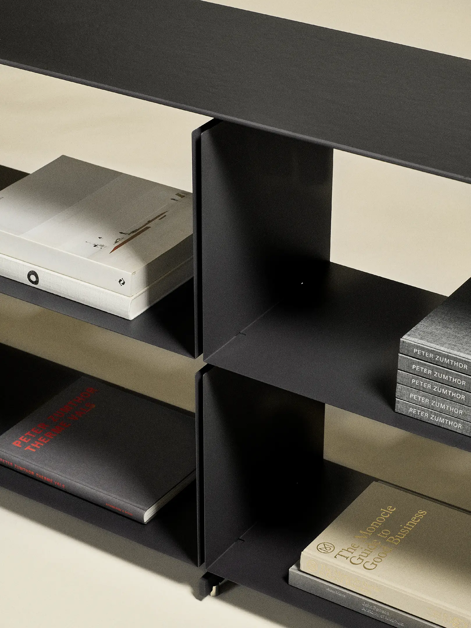 Black metal shelving with books arranged on lower shelves casting shadows on a light floor.