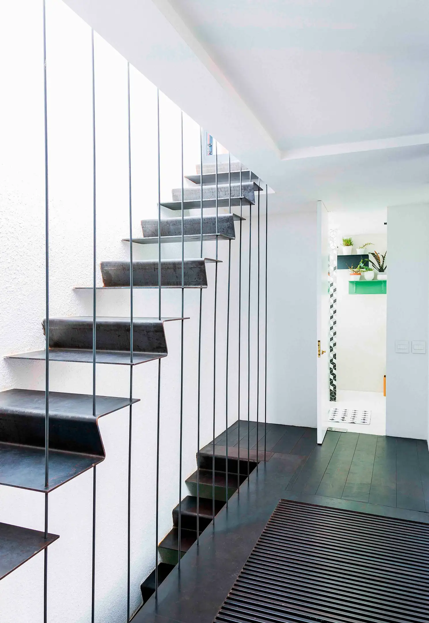 Minimalist black metal floating staircase with thin vertical railings next to a white wall and open door.