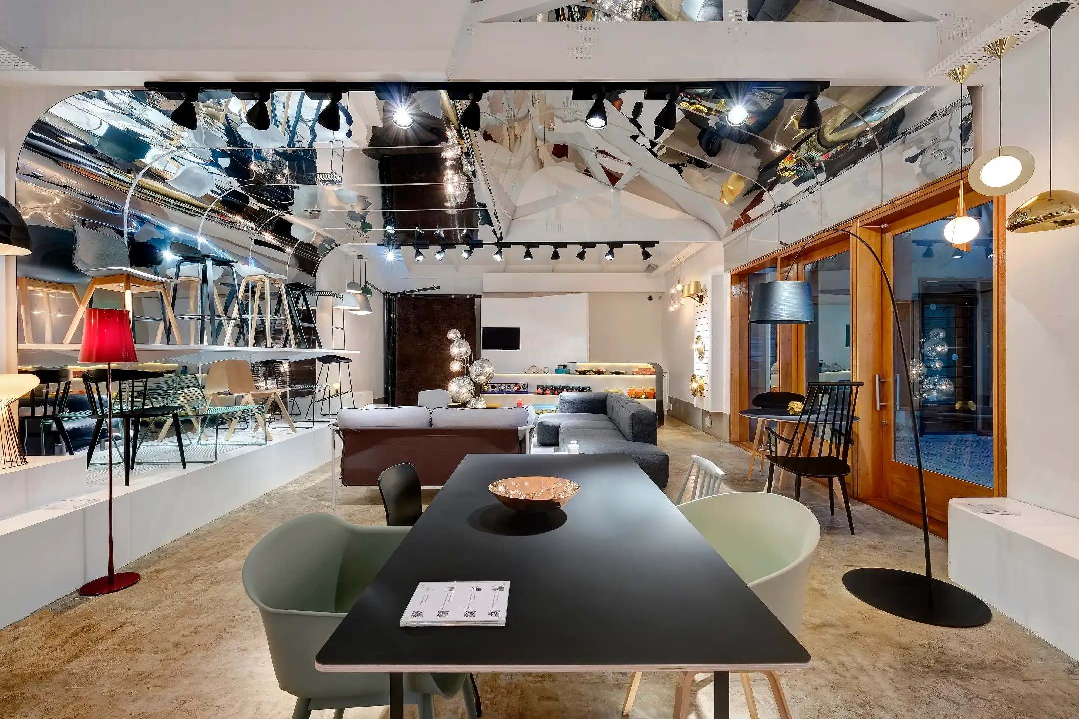 Modern showroom with black table, assorted chairs, sofas, metallic ceiling, and stylish lamps.