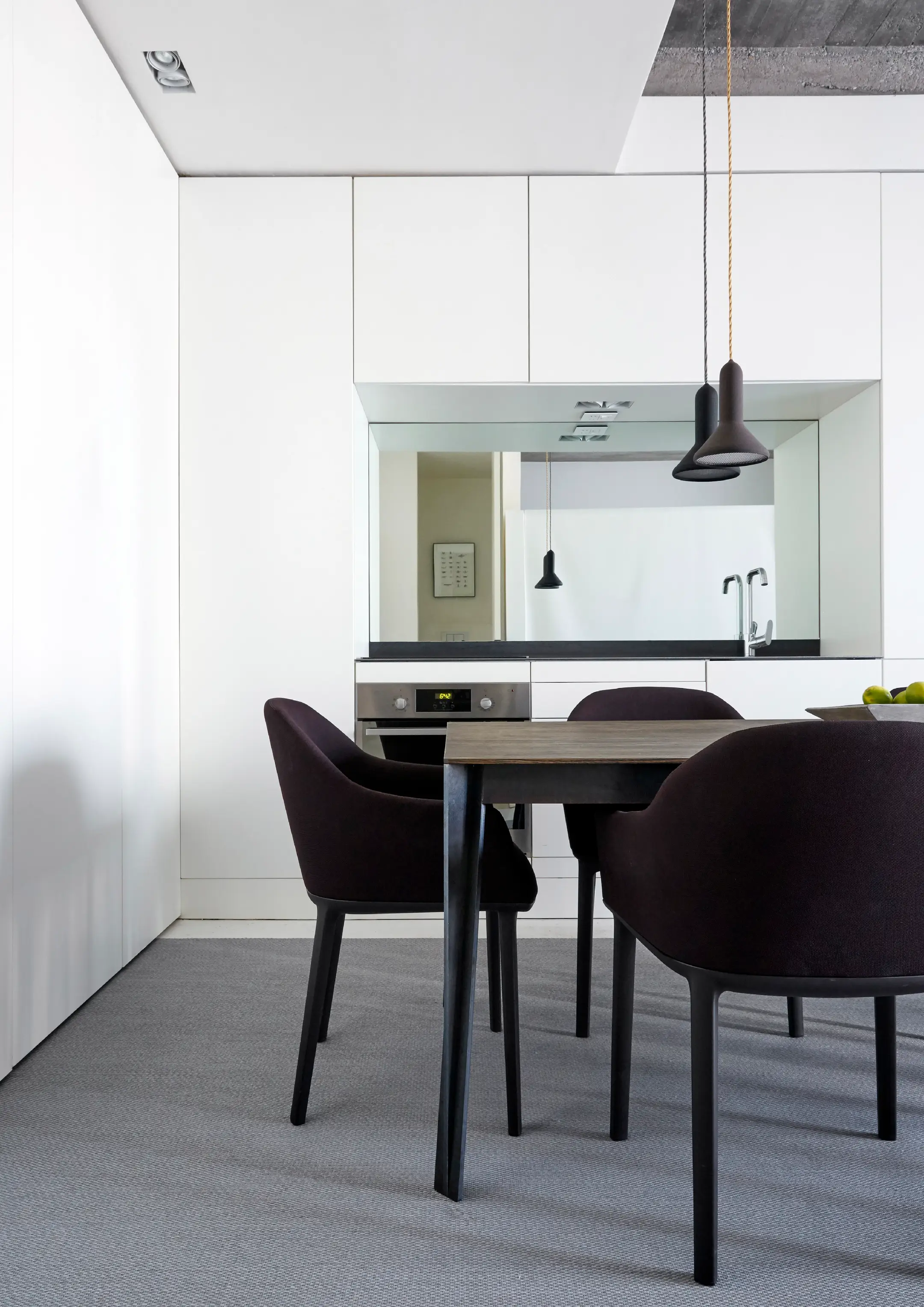 Minimalist dining area with black chairs, wooden table, white cabinets, and hanging pendant lights.