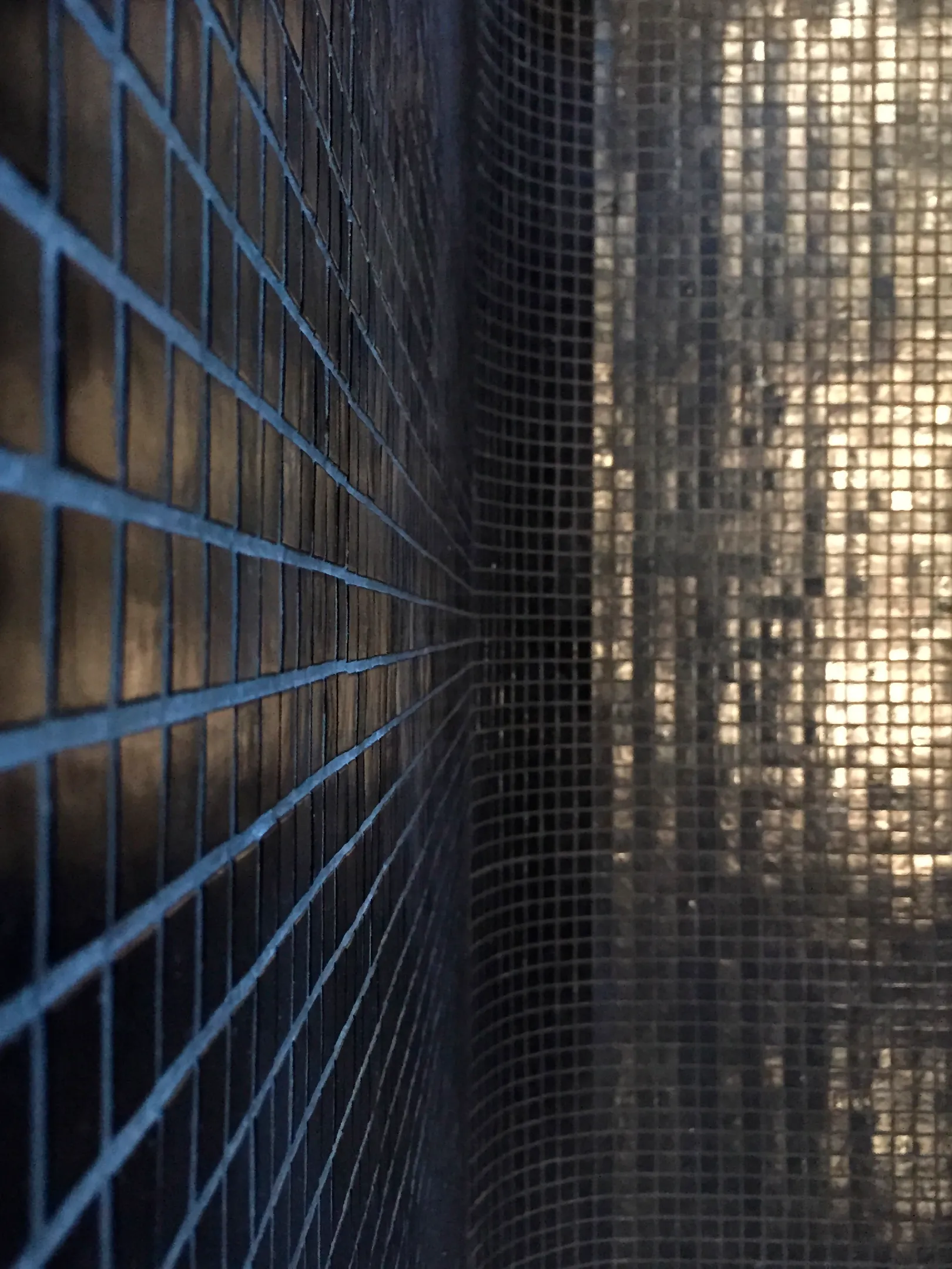 Close-up side view of two tiled walls meeting at a corner with reflective surfaces and grid patterns.