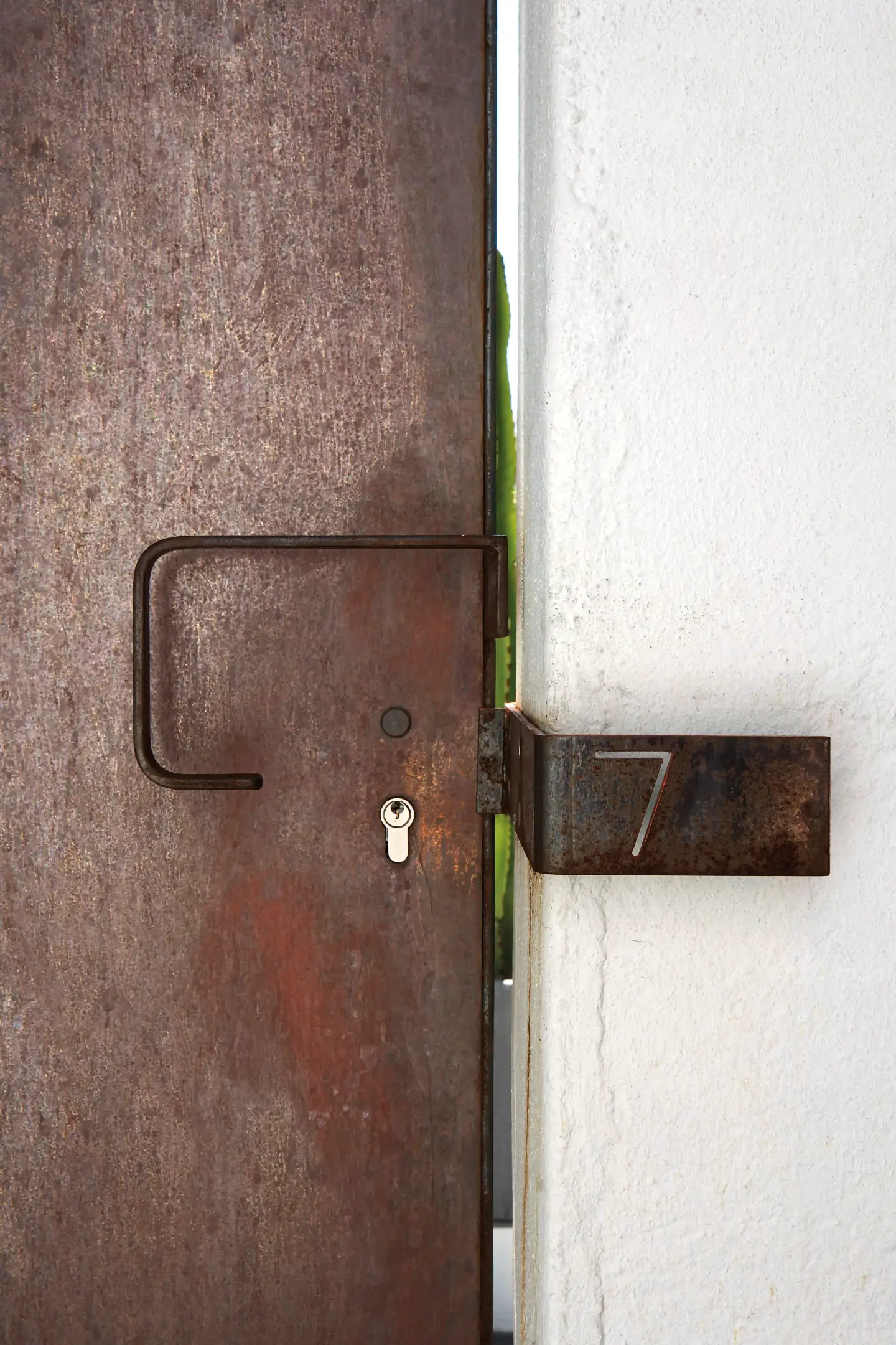 Rusty metal door with a simple handle and keyhole next to a white wall showing the number 7.
