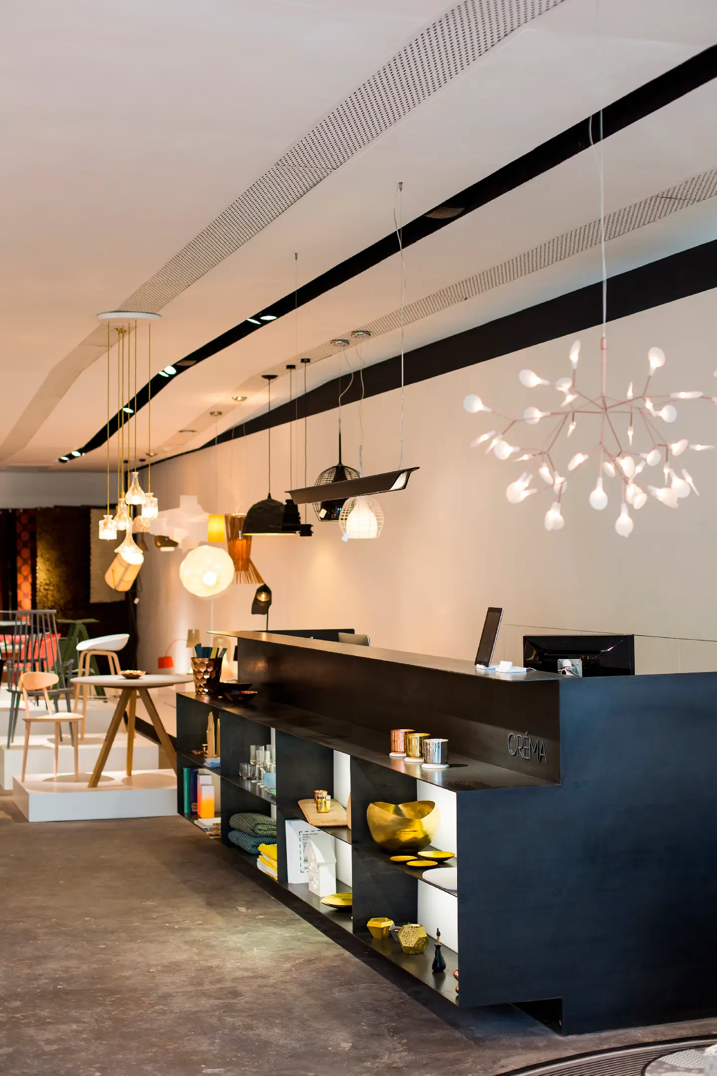 Modern furniture showroom with pendant lights, wooden chairs, and decorative items on shelves.
