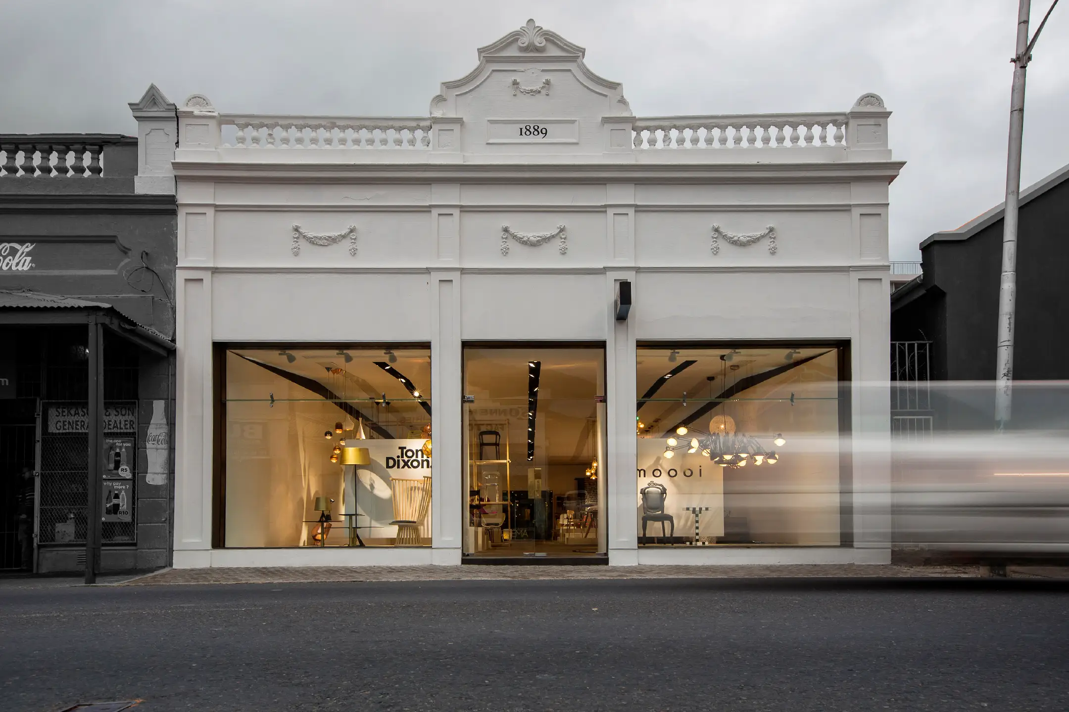 White historic building from 1889 with large glass windows showing modern interior lighting and furniture.