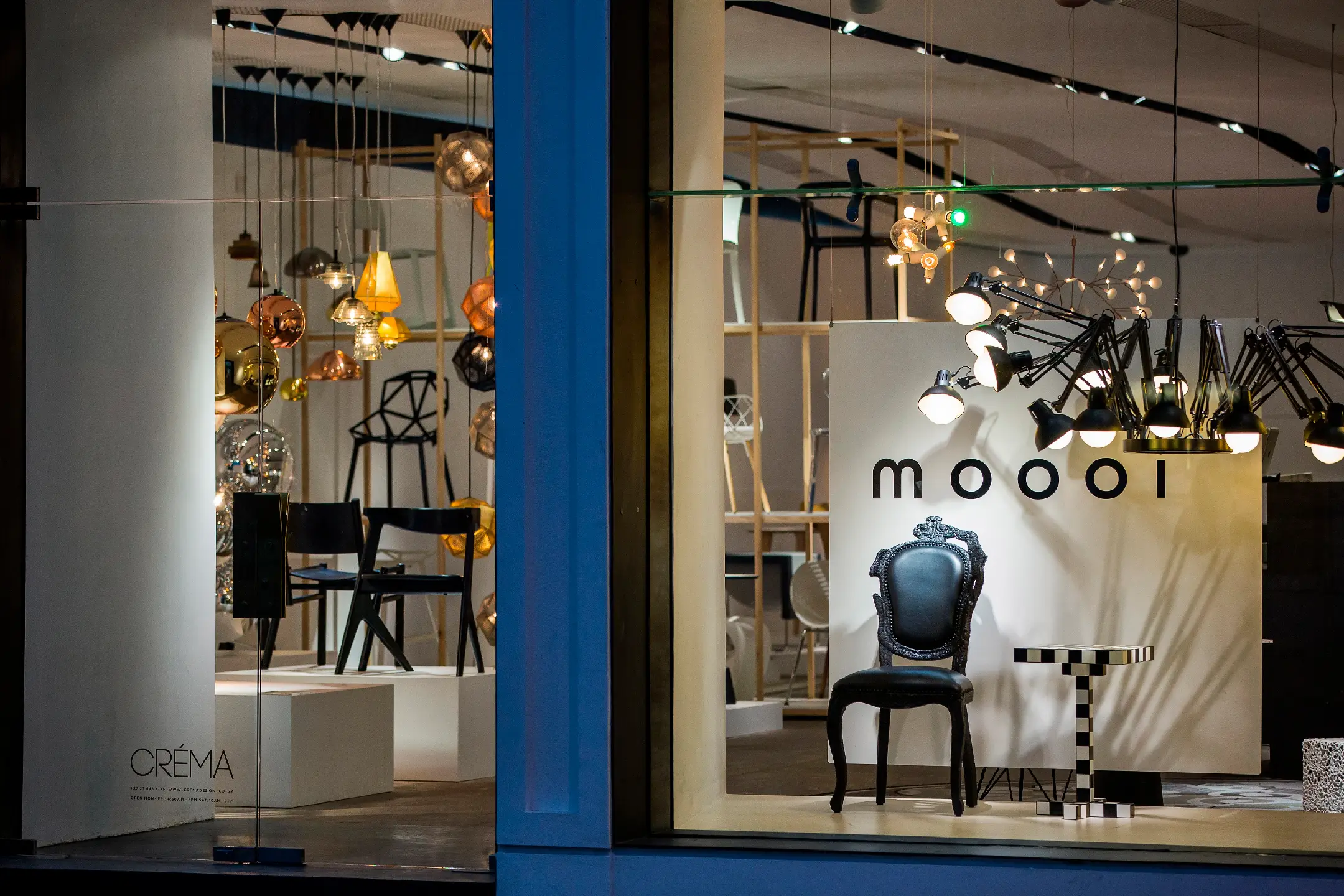 Modern furniture store window with black ornate chair, checkered table, and hanging lights.