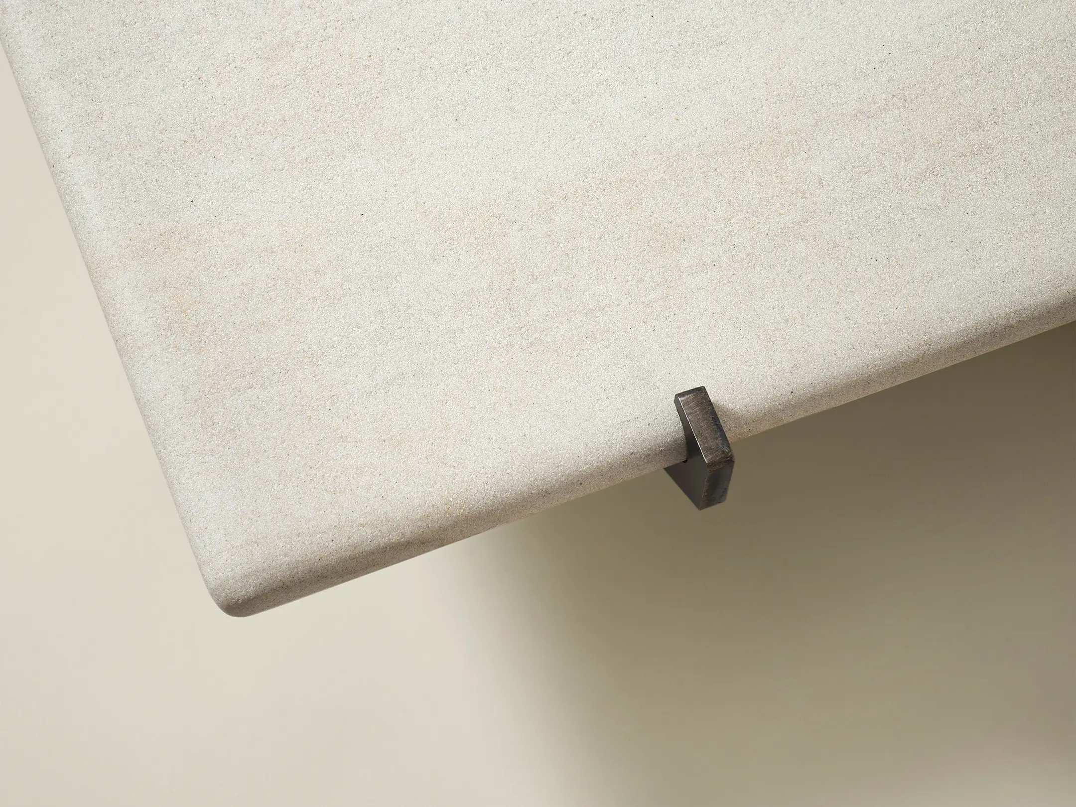Close-up of a textured beige stone tabletop with a small metal bracket underneath the edge.