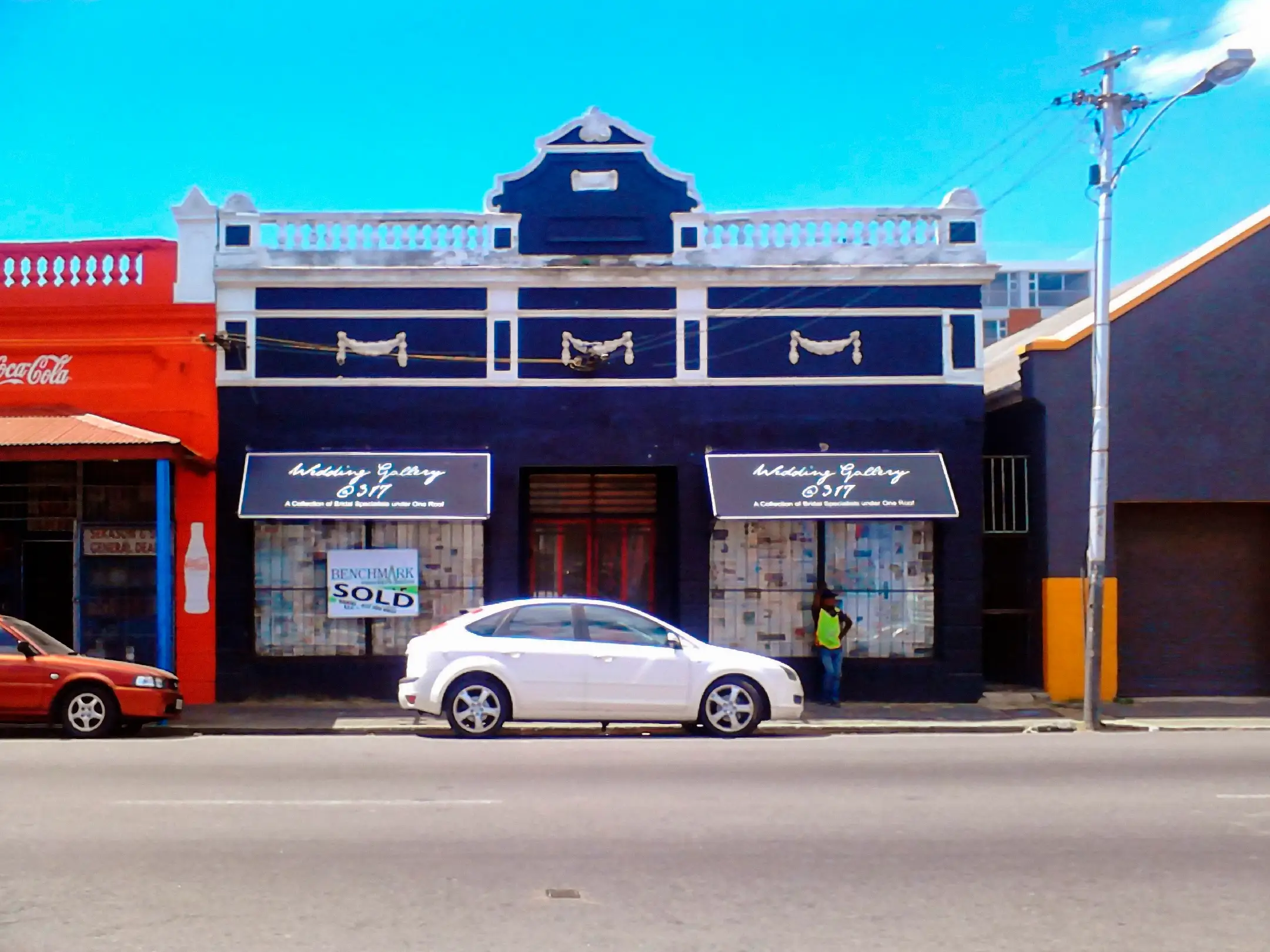 Street view of a dark blue building with Wedding Gallery signs and cars parked outside.