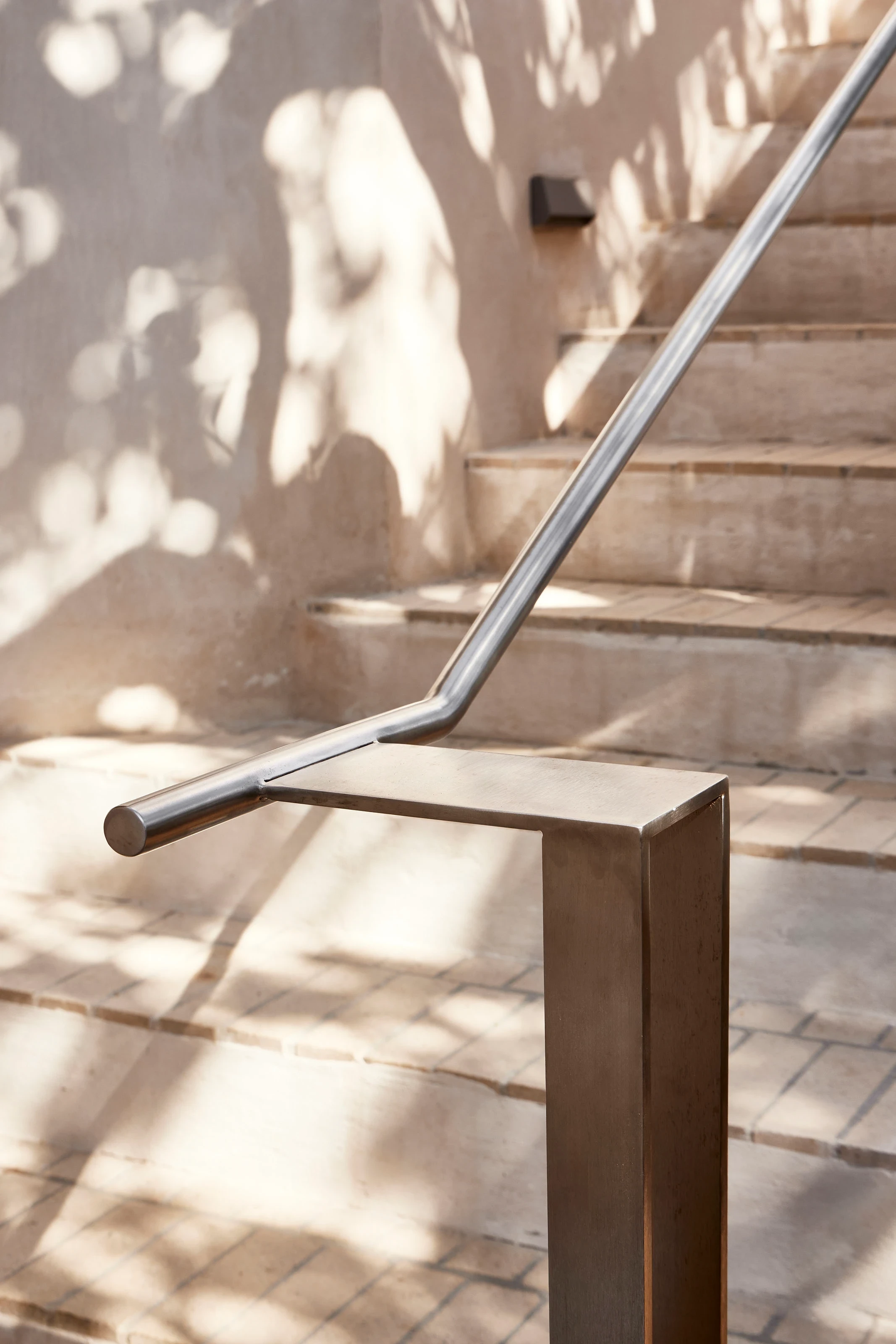 Modern stainless steel handrail on light stone steps with soft shadows on the wall.