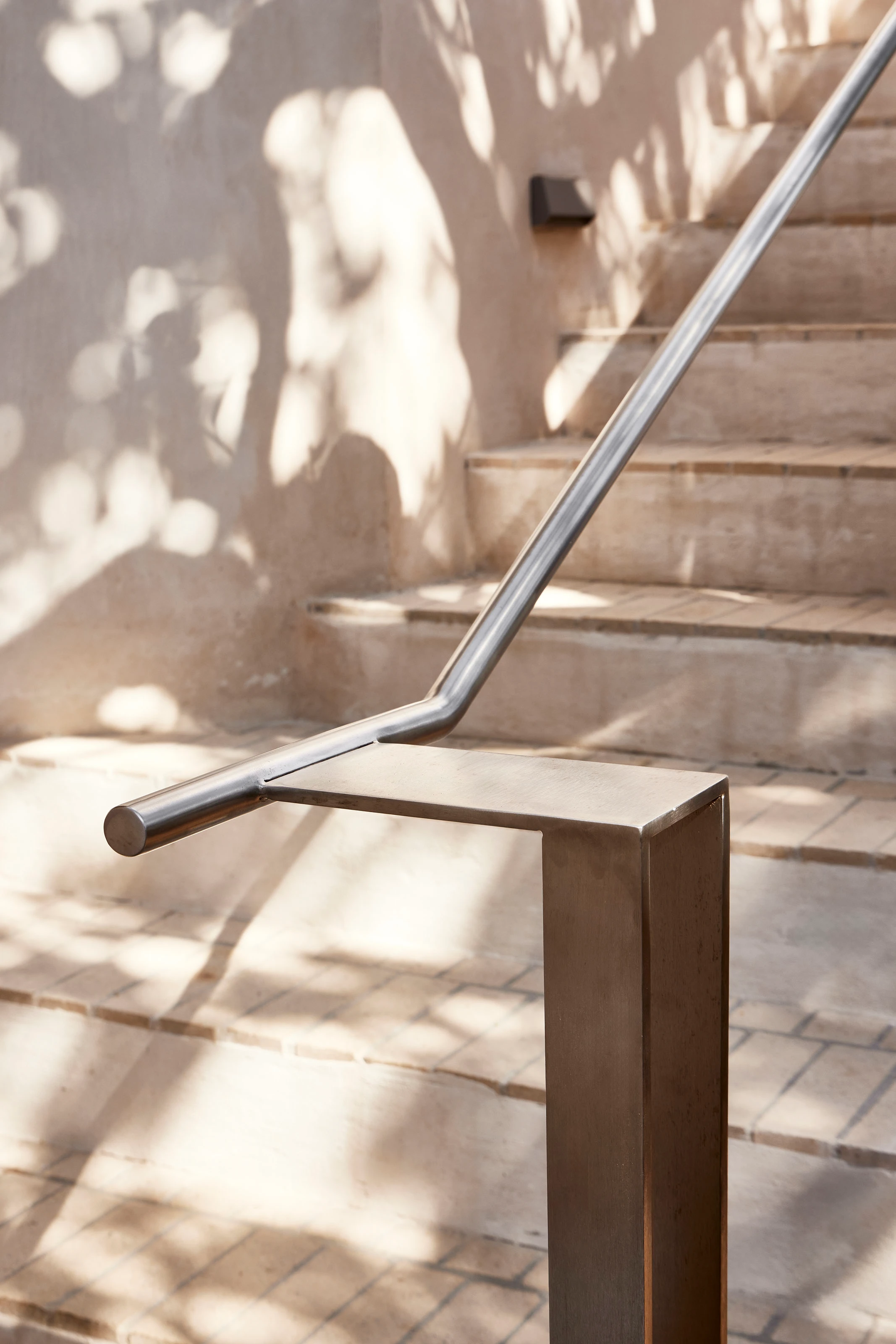Modern stainless steel handrail on light stone steps with soft shadows on the wall.