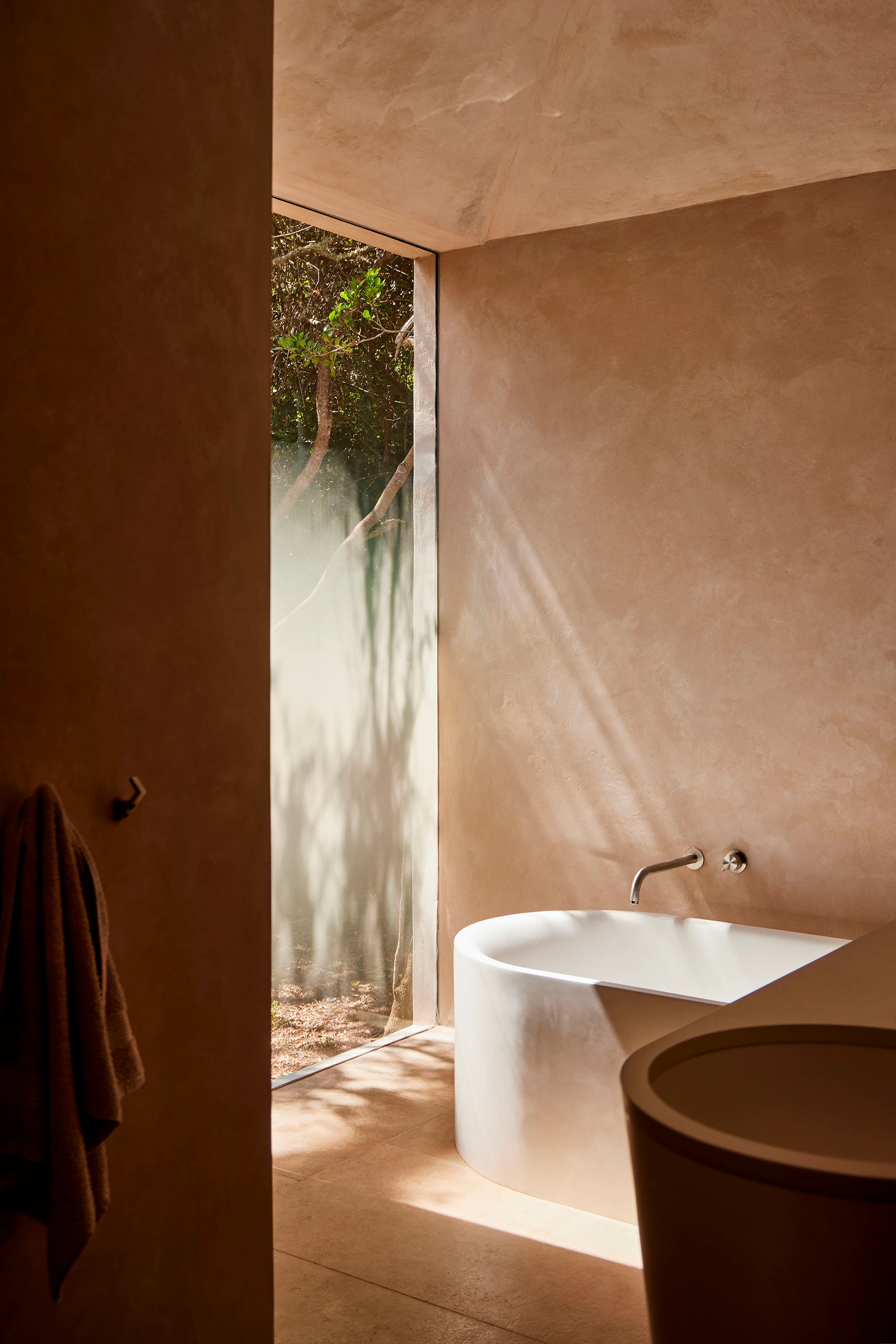 Modern bathroom with white tub, beige walls, and frosted window showing outdoor greenery.