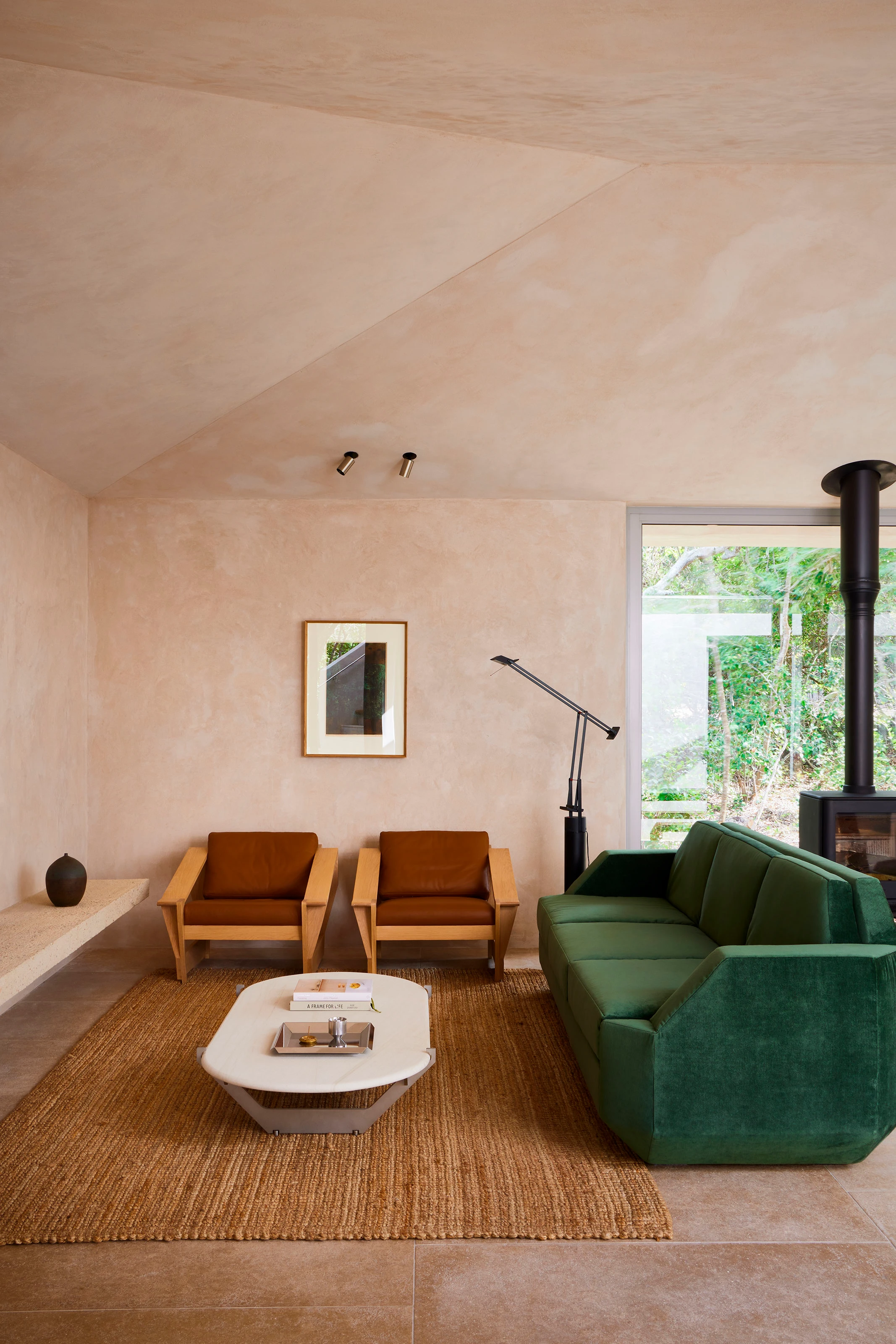 Minimalist living room with green sofa, two brown leather armchairs, white coffee table, and large window.