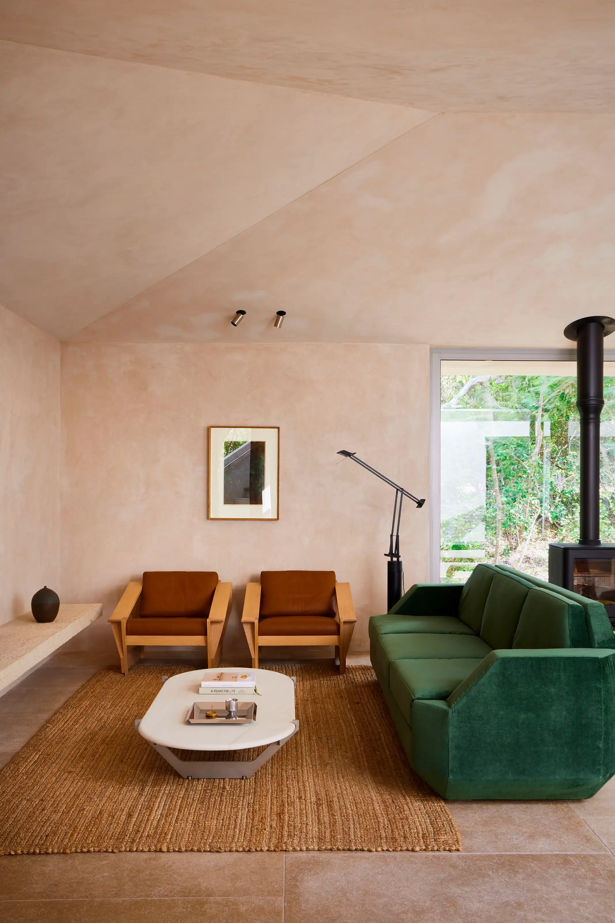 Minimalist living room with green sofa, two brown leather armchairs, white coffee table, and large window.