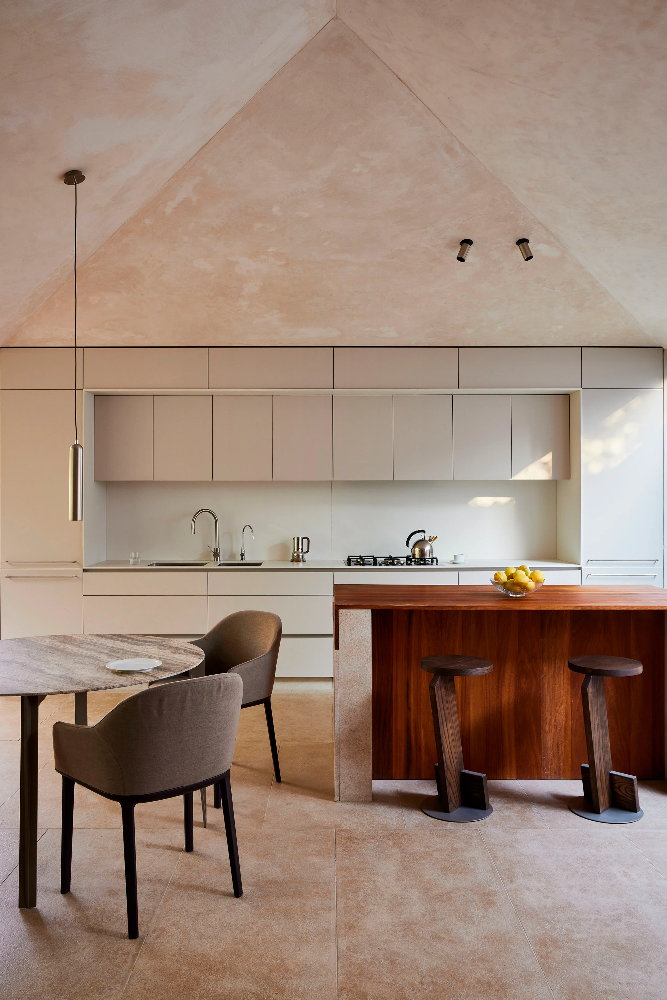 Minimalist kitchen with beige cabinets, wooden island with stools, round table, and pendant light.