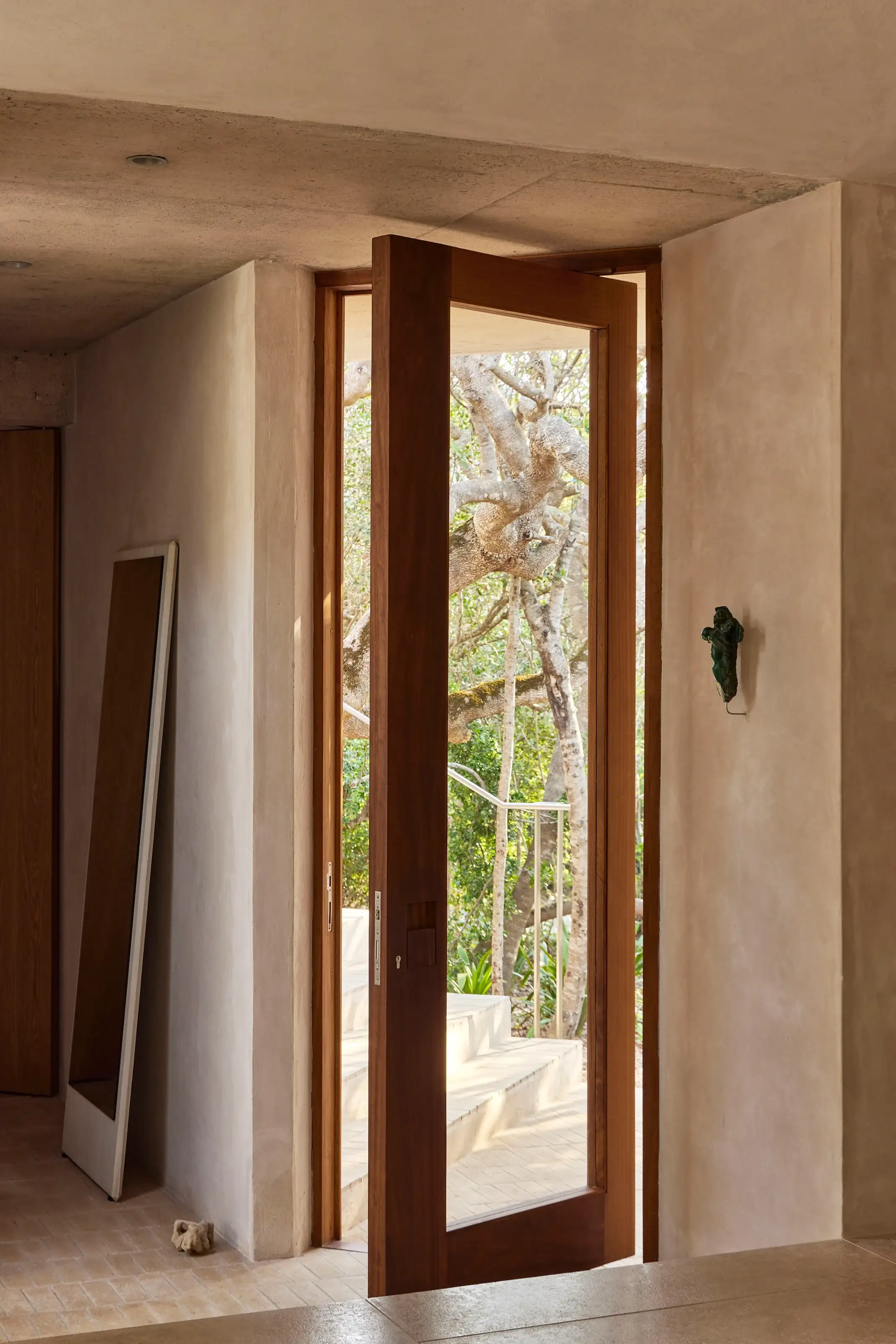 Wood-framed glass door opens to outdoor steps with trees visible outside in natural light.