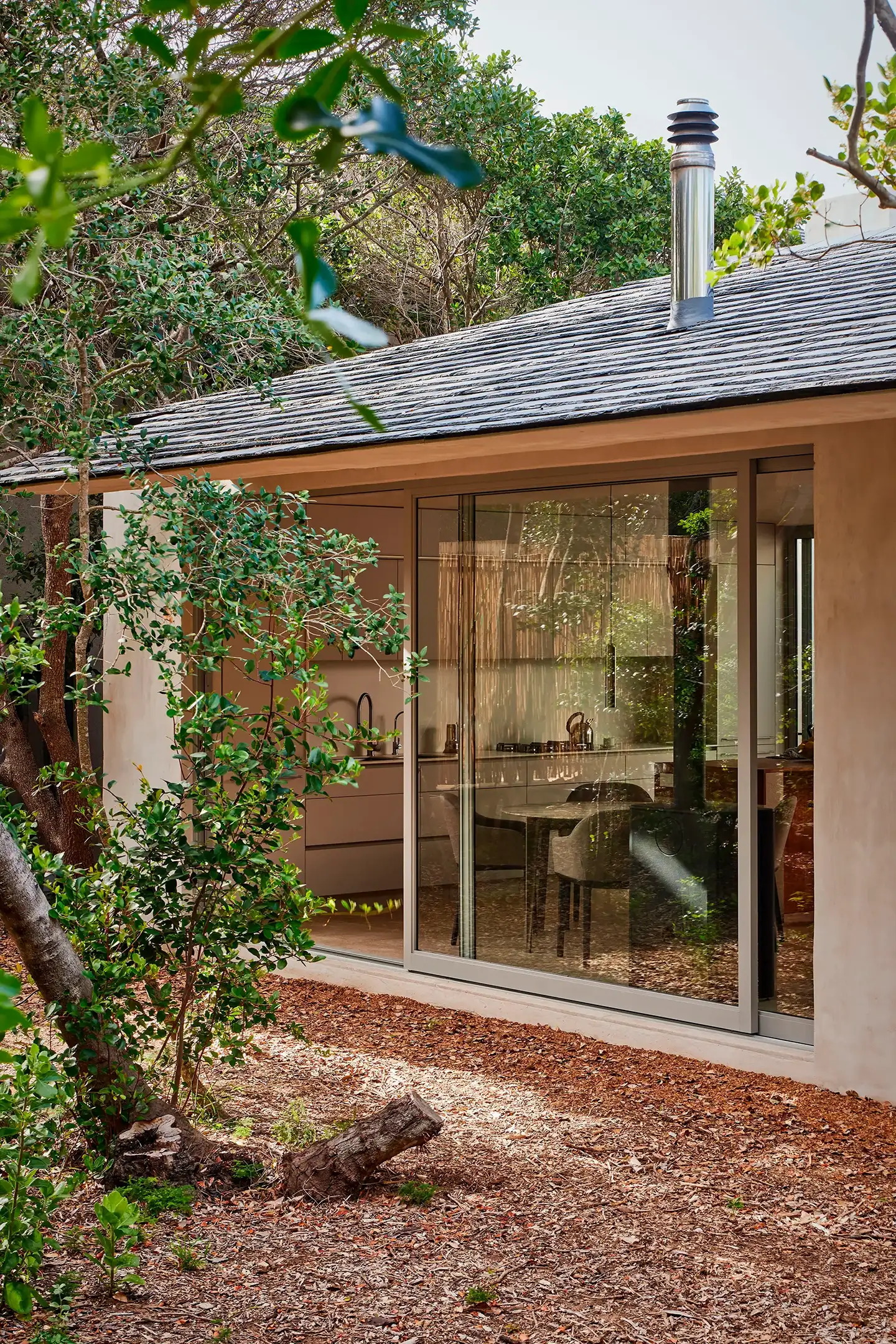 Modern house exterior with large glass sliding doors showing a kitchen and dining area inside.