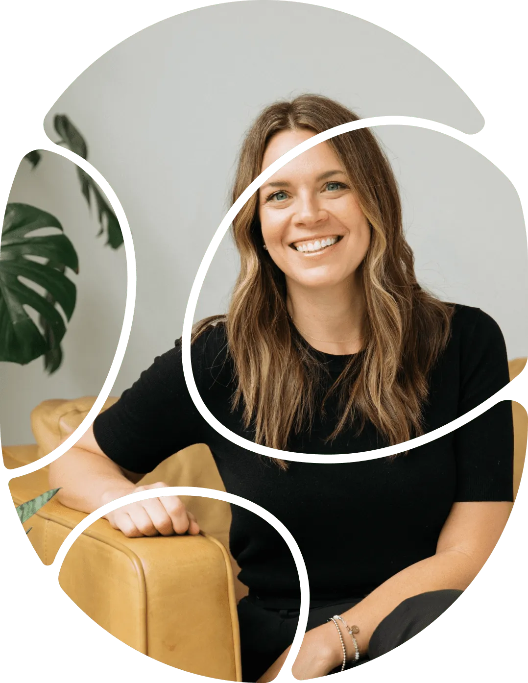 Smiling woman with long light brown hair wearing a black shirt sitting on a tan leather chair with a green plant in the background.