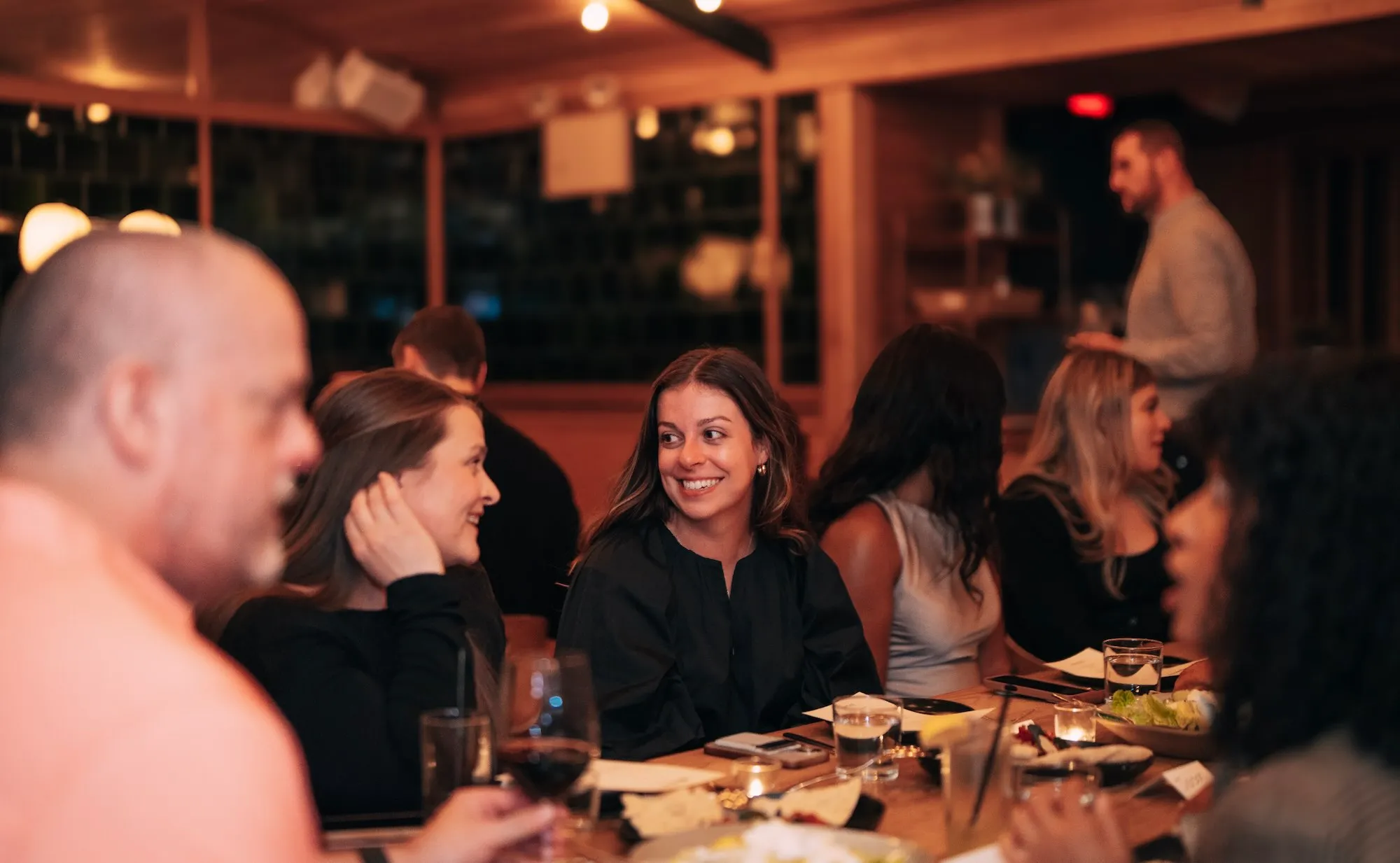 Group of people dining and smiling together at a warm, cozy restaurant table.