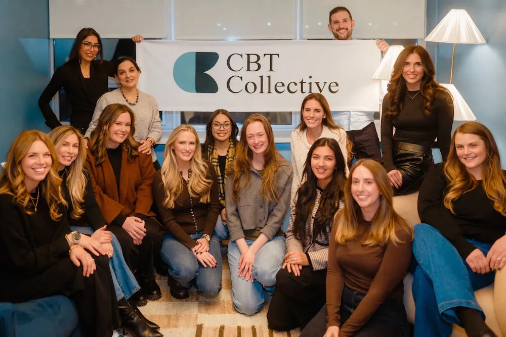 Group of smiling people posing indoors with a banner reading 'CBT Collective'.
