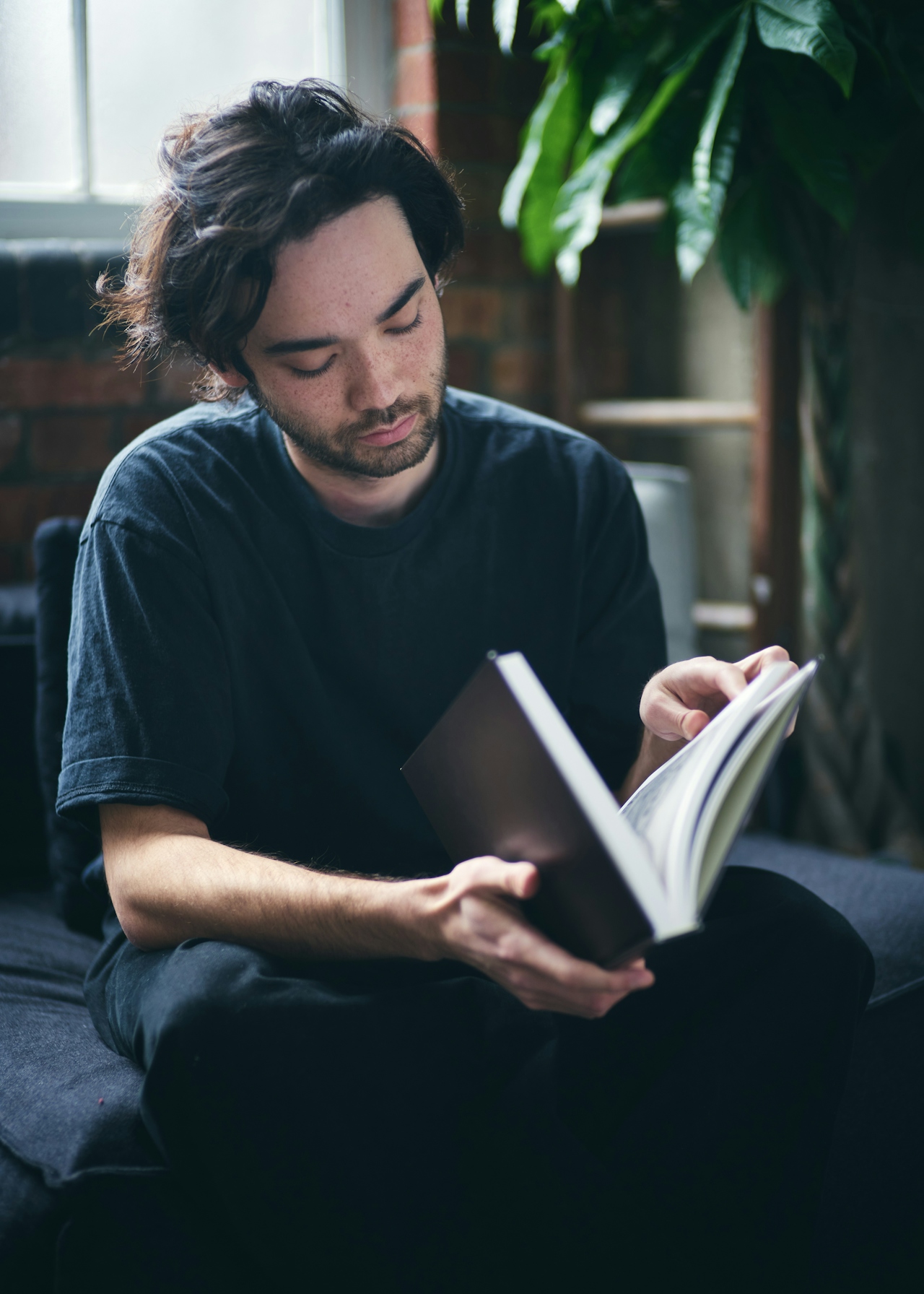 Jeune homme aux cheveux bruns et fournis lisant un livre, illustrant l'attention portée à la santé et au bien-être capillaire.