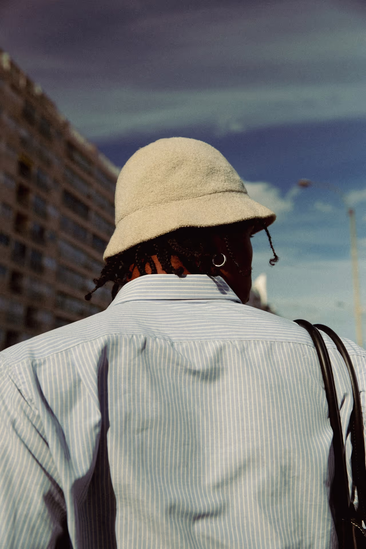 Personne de dos avec chapeau bob beige, tresses et chemise rayée. Image illustrative de coiffures et couvre-chefs.