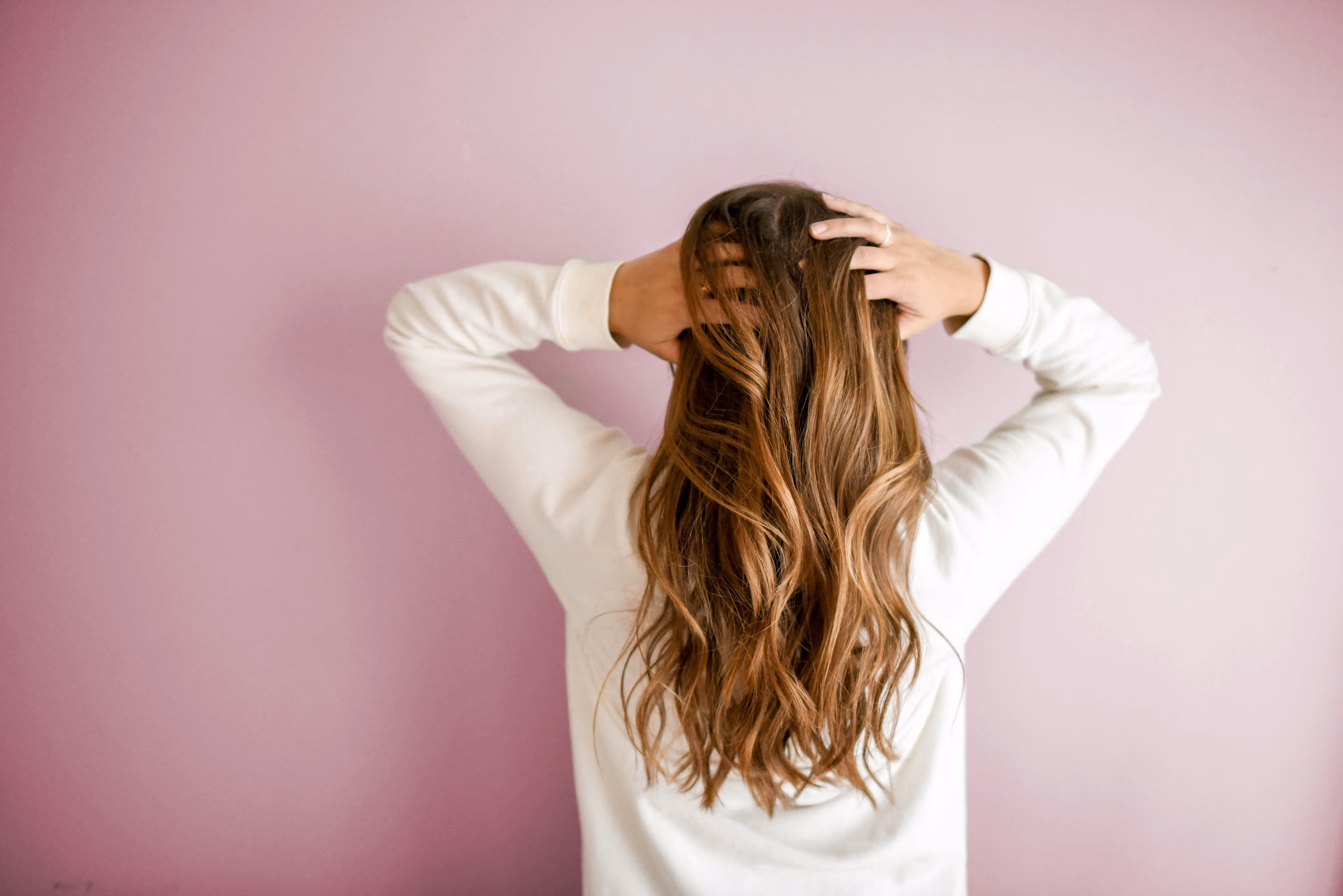 Femme aux cheveux châtains ondulés, vue de dos, prenant soin de sa chevelure, en lien avec la santé capillaire.