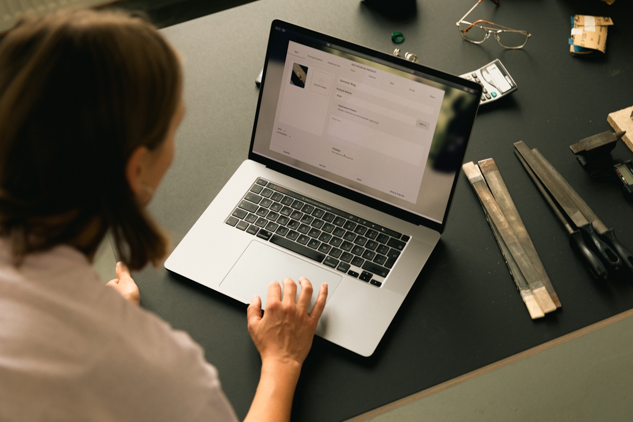 Femme travaillant sur un ordinateur portable, écran affichant une interface digitale, outils et accessoires sur une table noire. Soutien professionnel.