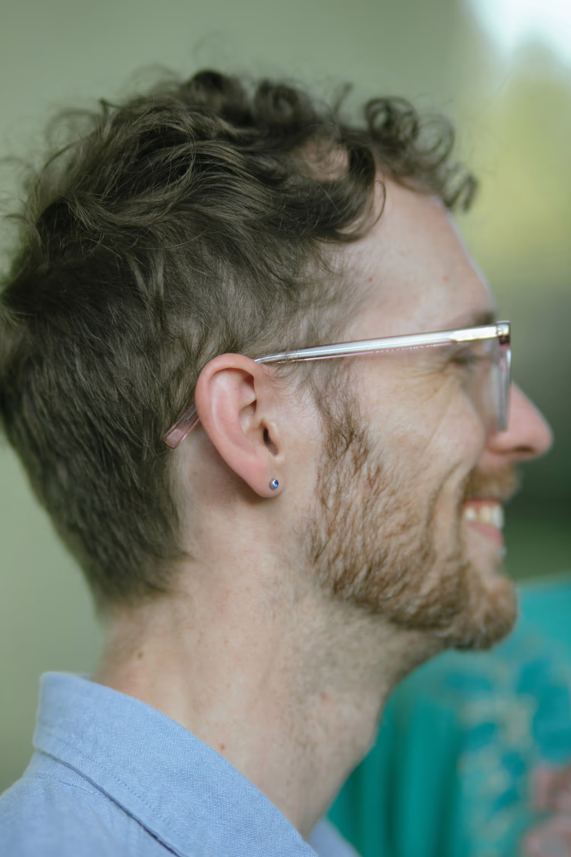 Homme souriant avec cheveux bouclés et barbe, portant des lunettes. Image pertinente pour la prise en charge de l'alopécie.